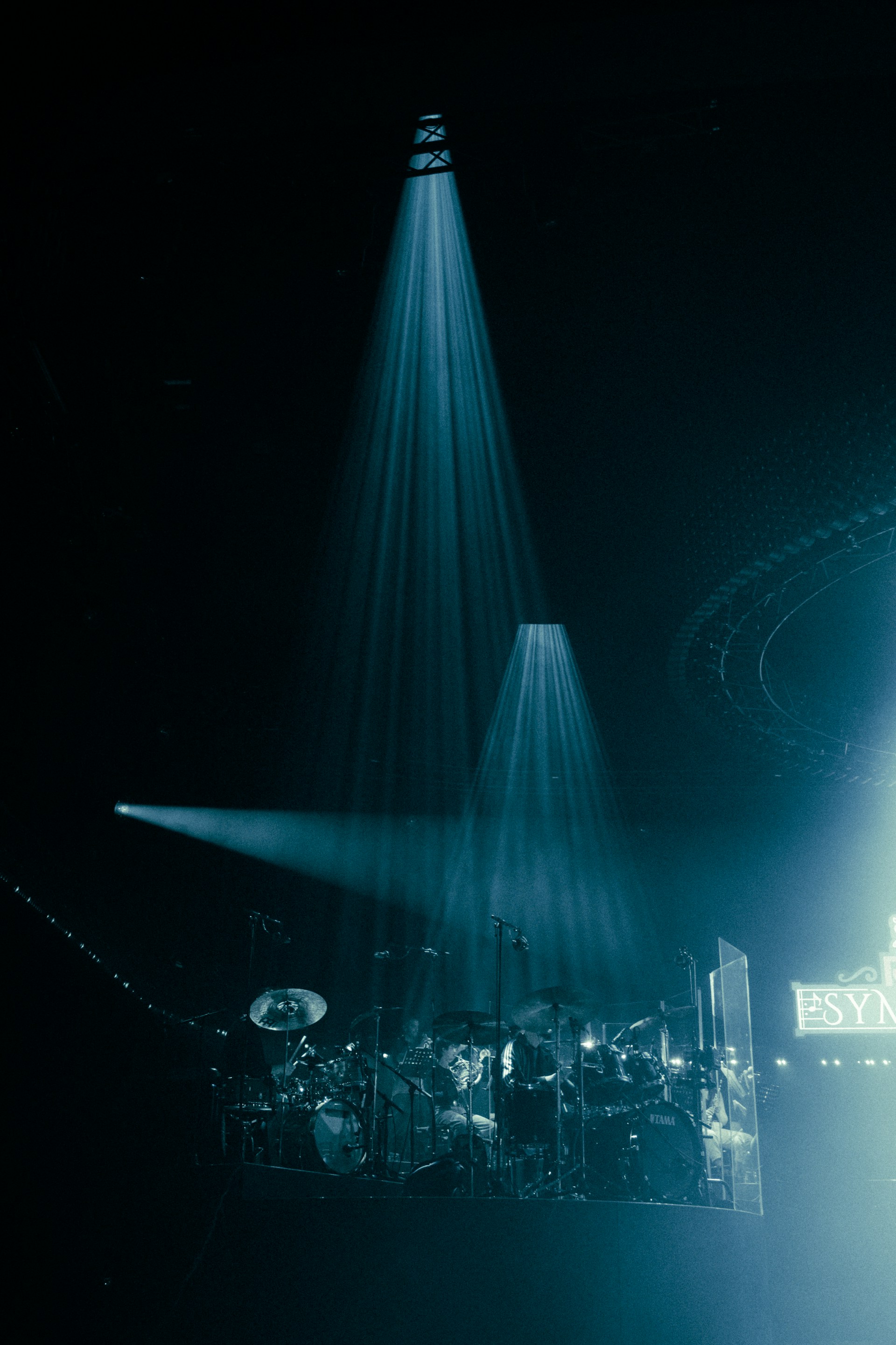 Drum set illuminated by spotlights on a dark stage.