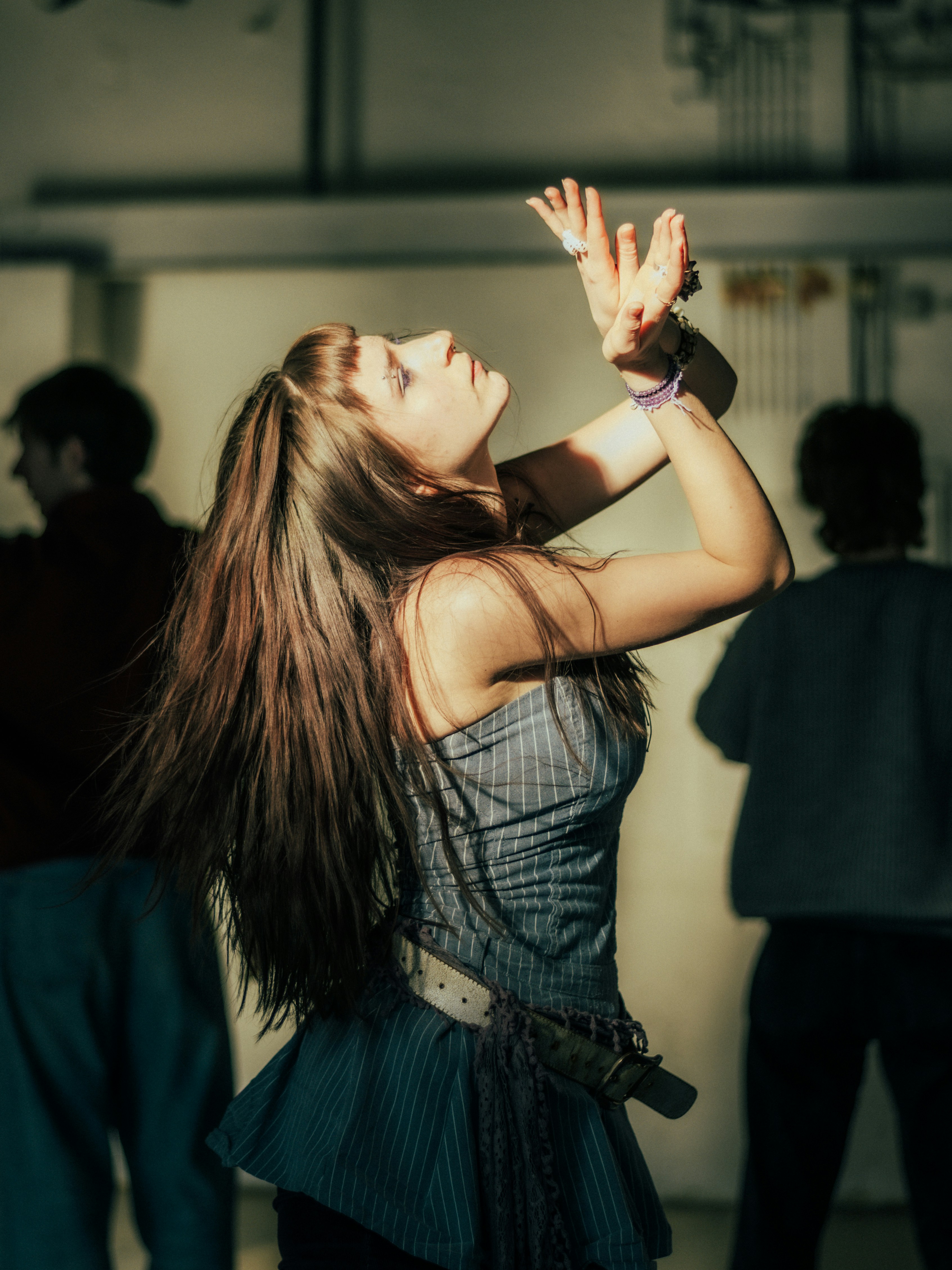 Young woman dancing with arms raised in dim lighting.