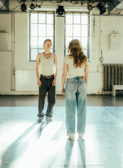 Two people stand in a sunlit room.