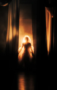 Silhouette of a woman in a glowing dress behind curtains