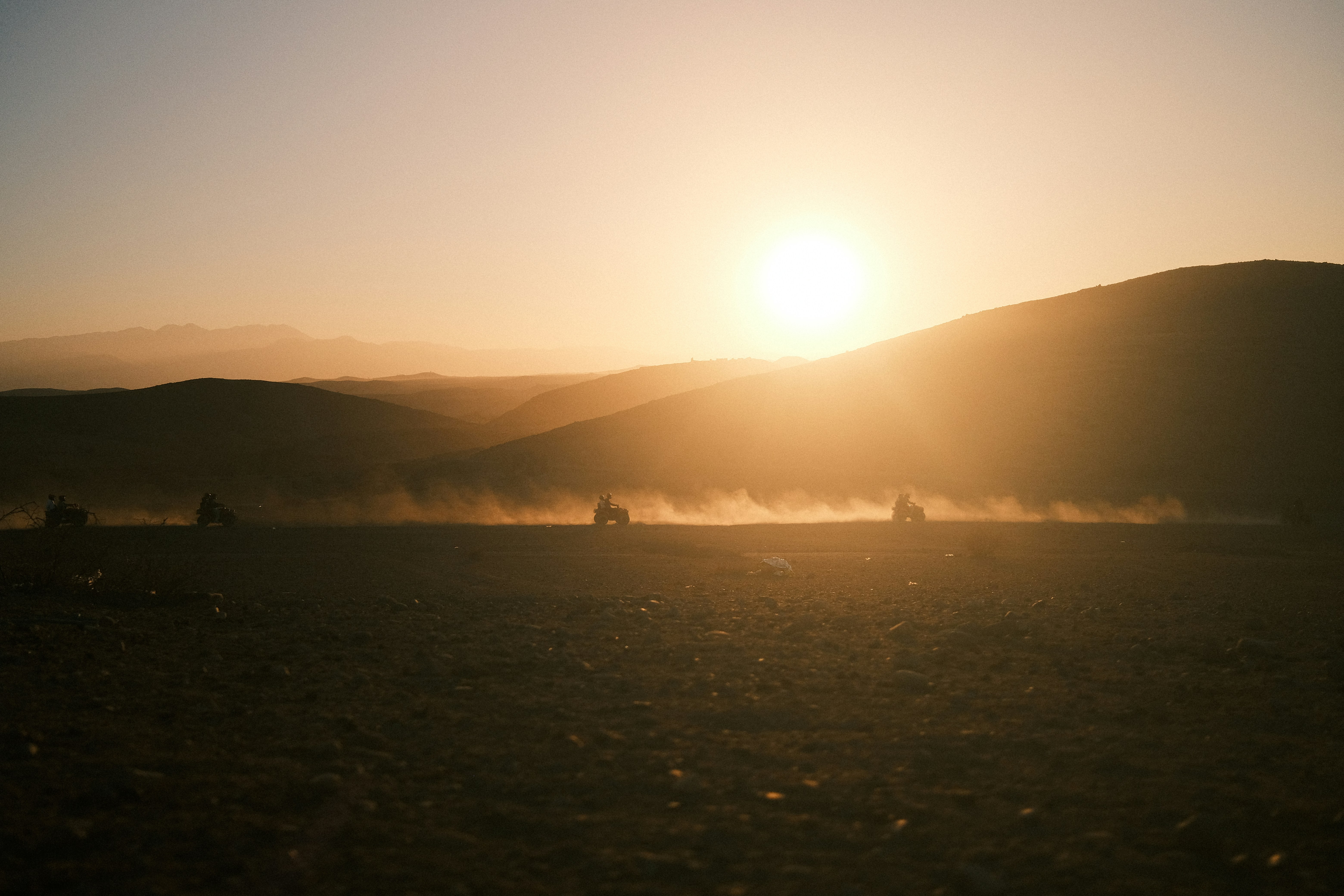 Dust kicks up behind vehicles in a desert at sunset.