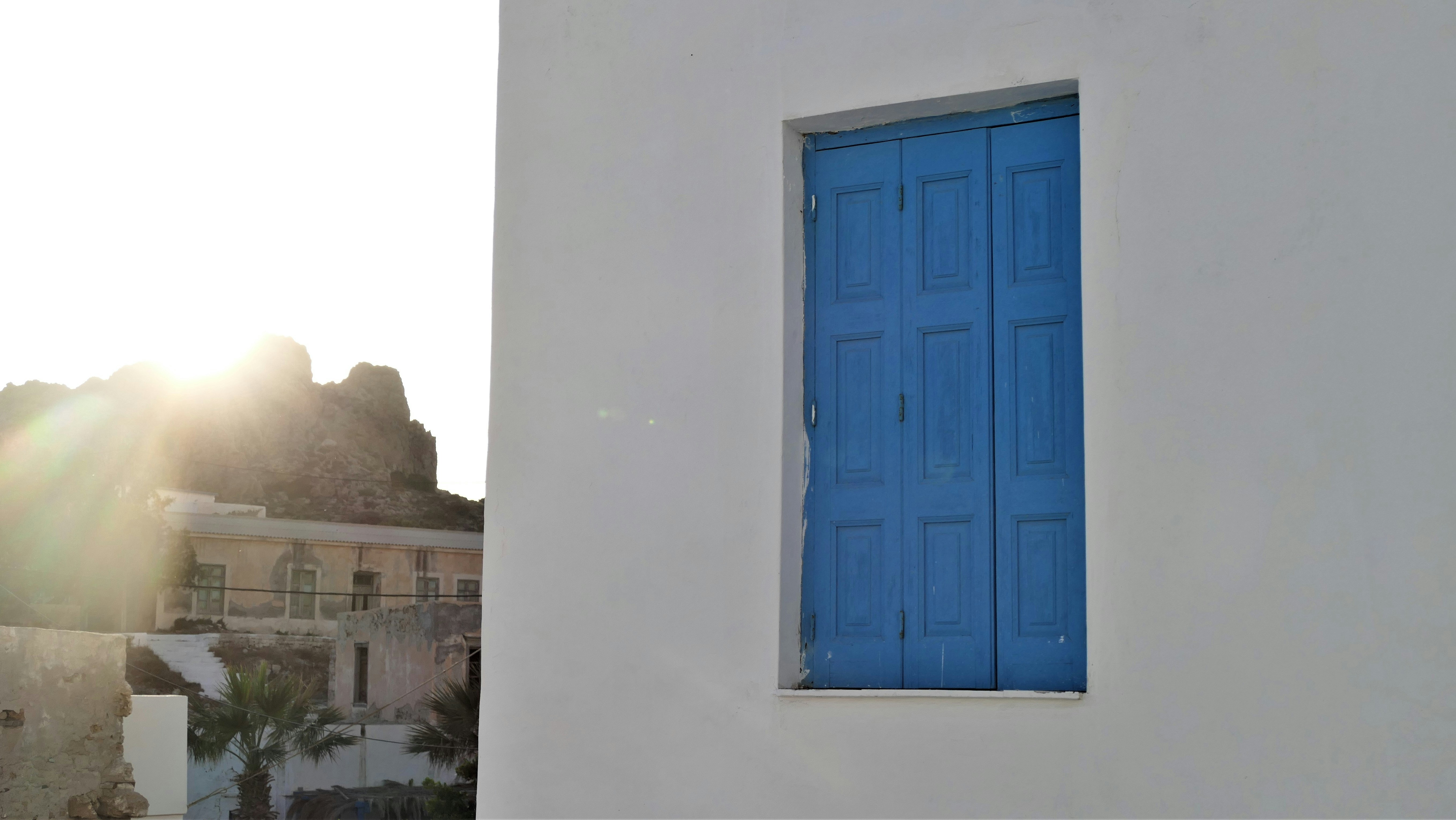 White building with blue shutters and sunlit hills.