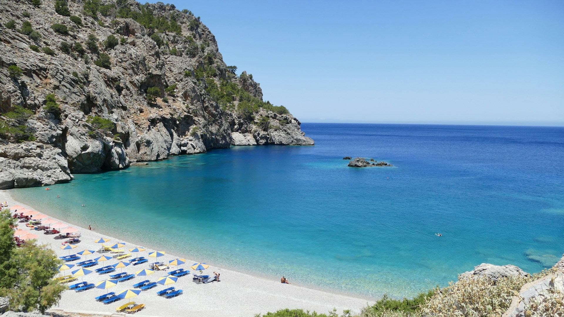 A scenic beach with clear blue water and rocky cliffs.