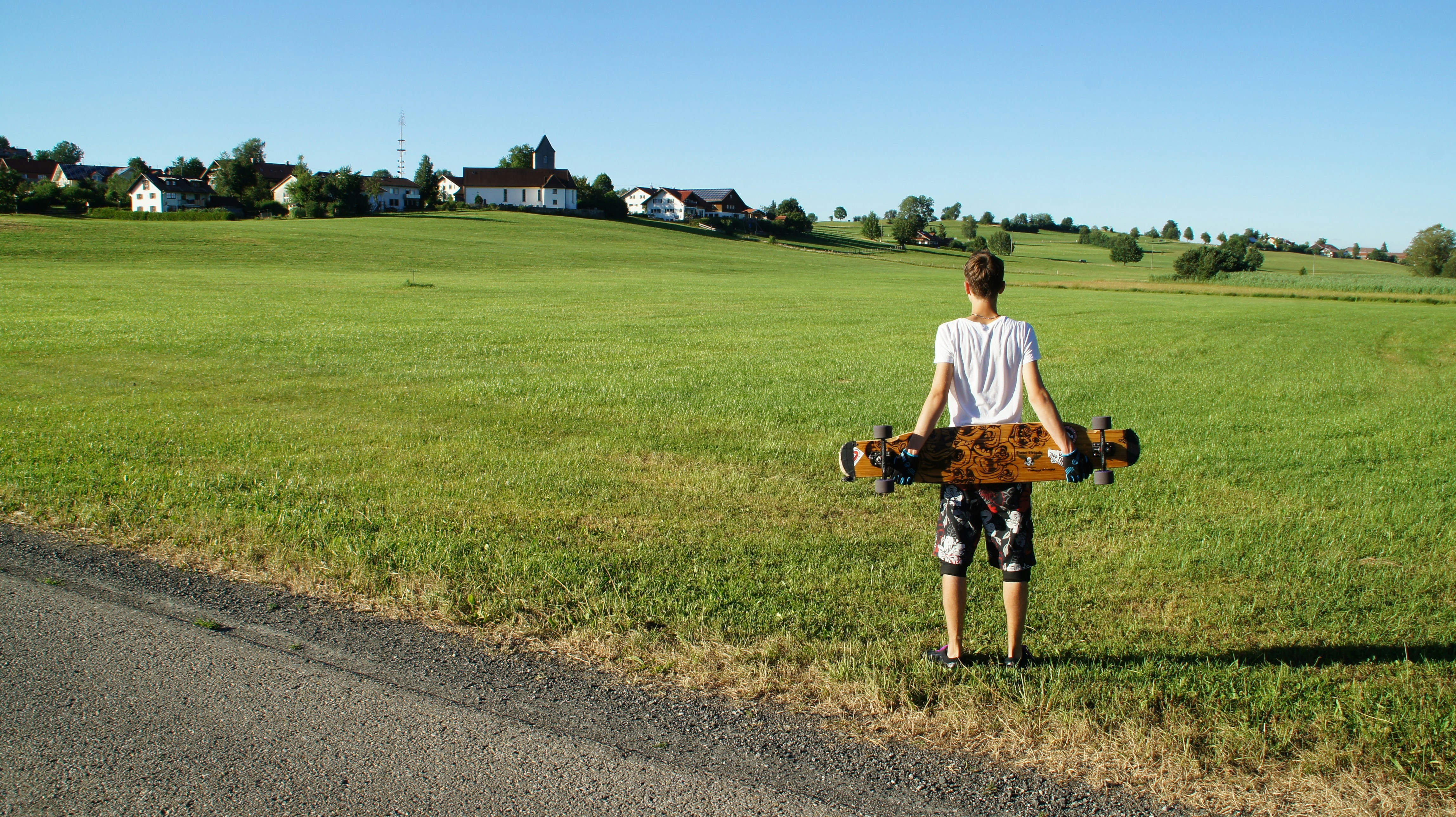 Young person holding longboard in grassy field 풍경 사진