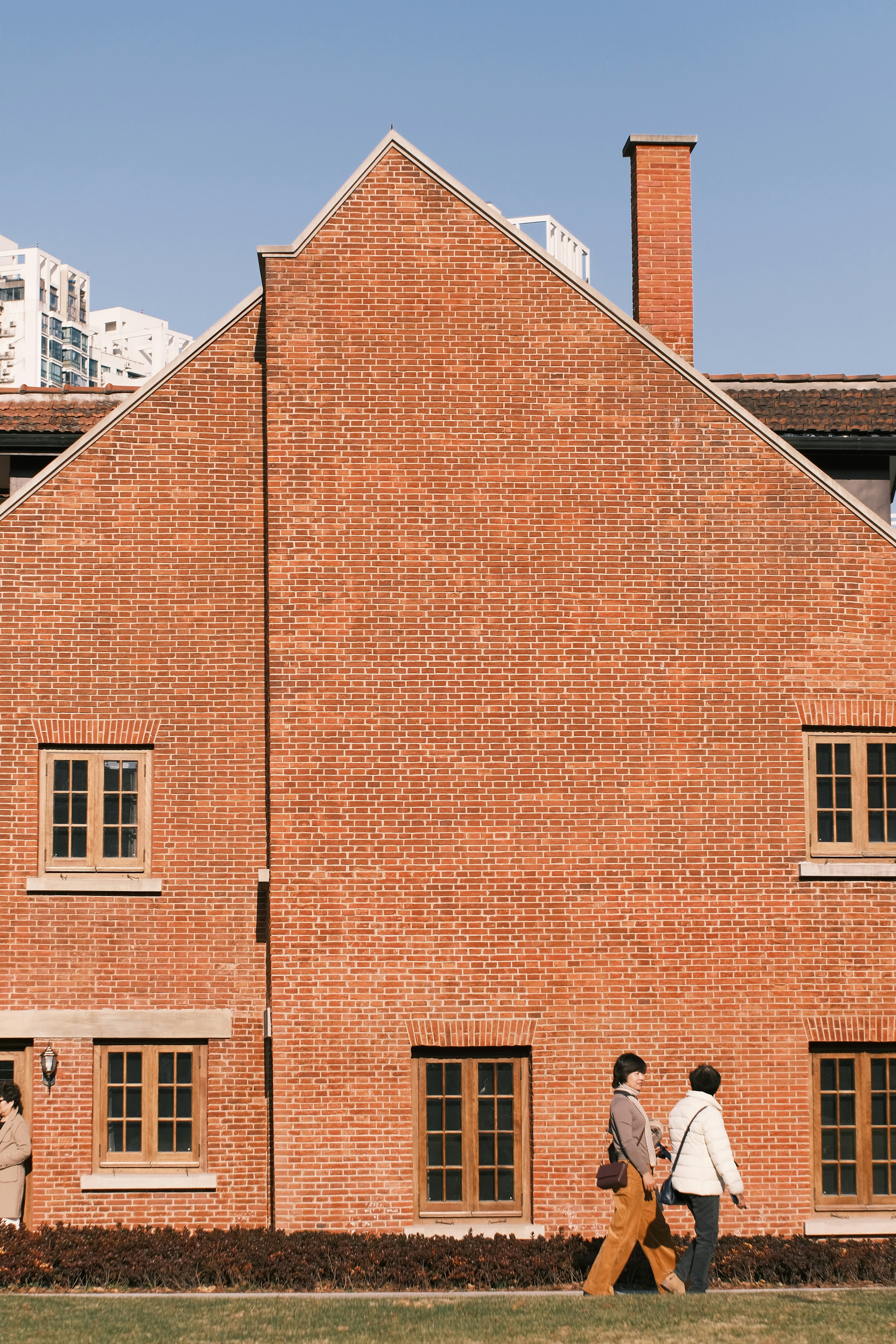Two people walk past a large brick building.