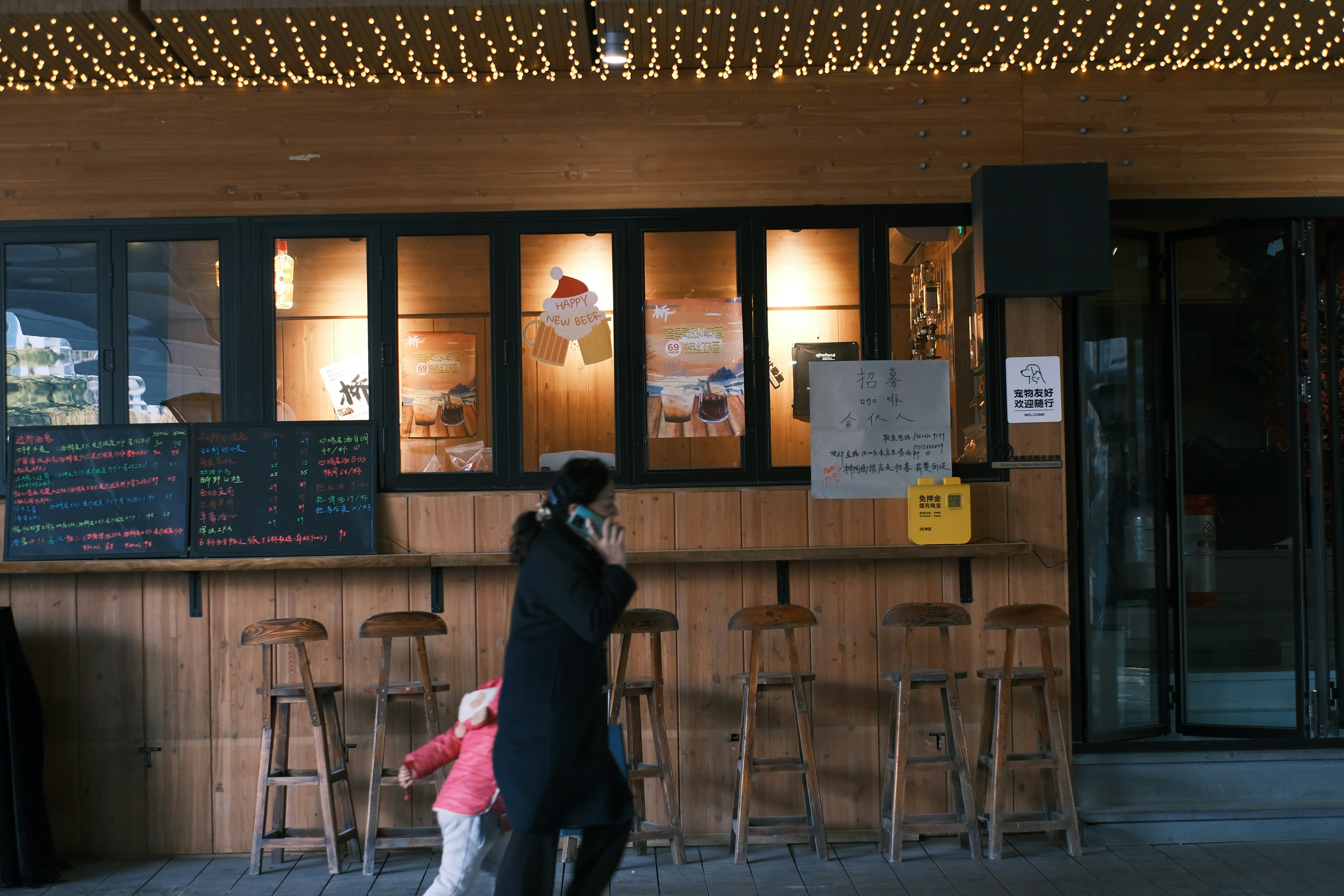 People walk past a bar with festive lights