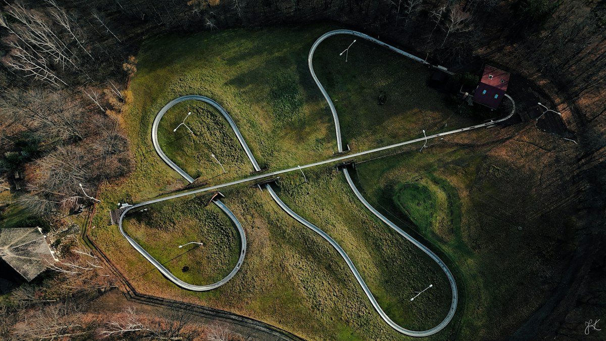 Overhead view of a coaster rail snaking in tight switchbacks through dense green forest