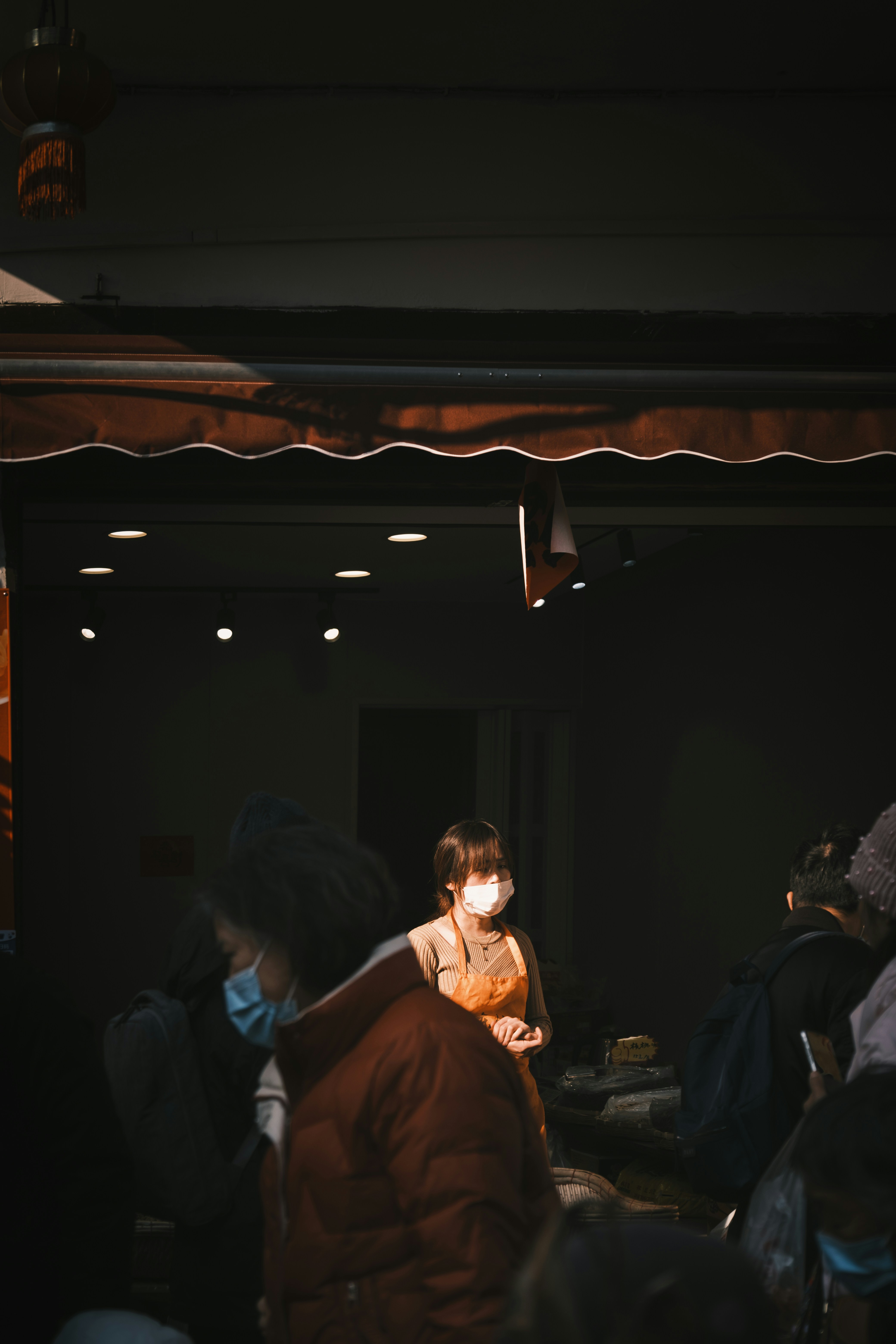 Woman wearing mask stands in dimly lit shop