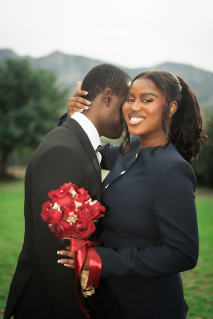 A smiling couple holding a red rose bouquet
