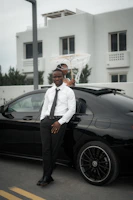 Man in suit poses by a black car
