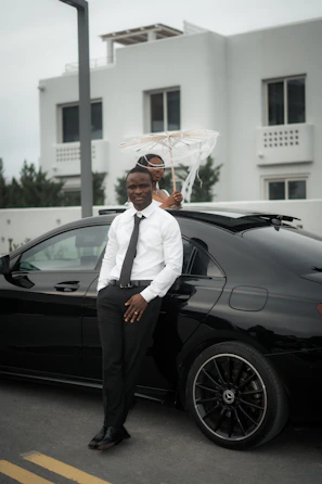 Man in suit poses by a black car