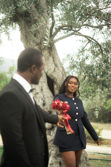 Man in tuxedo gives woman flowers by olive tree.