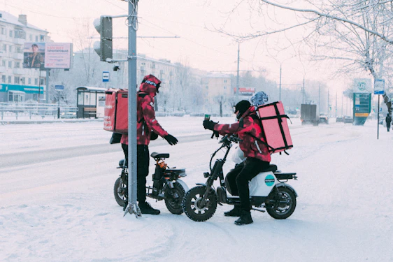 Delivery workers on scooters in snowy city street