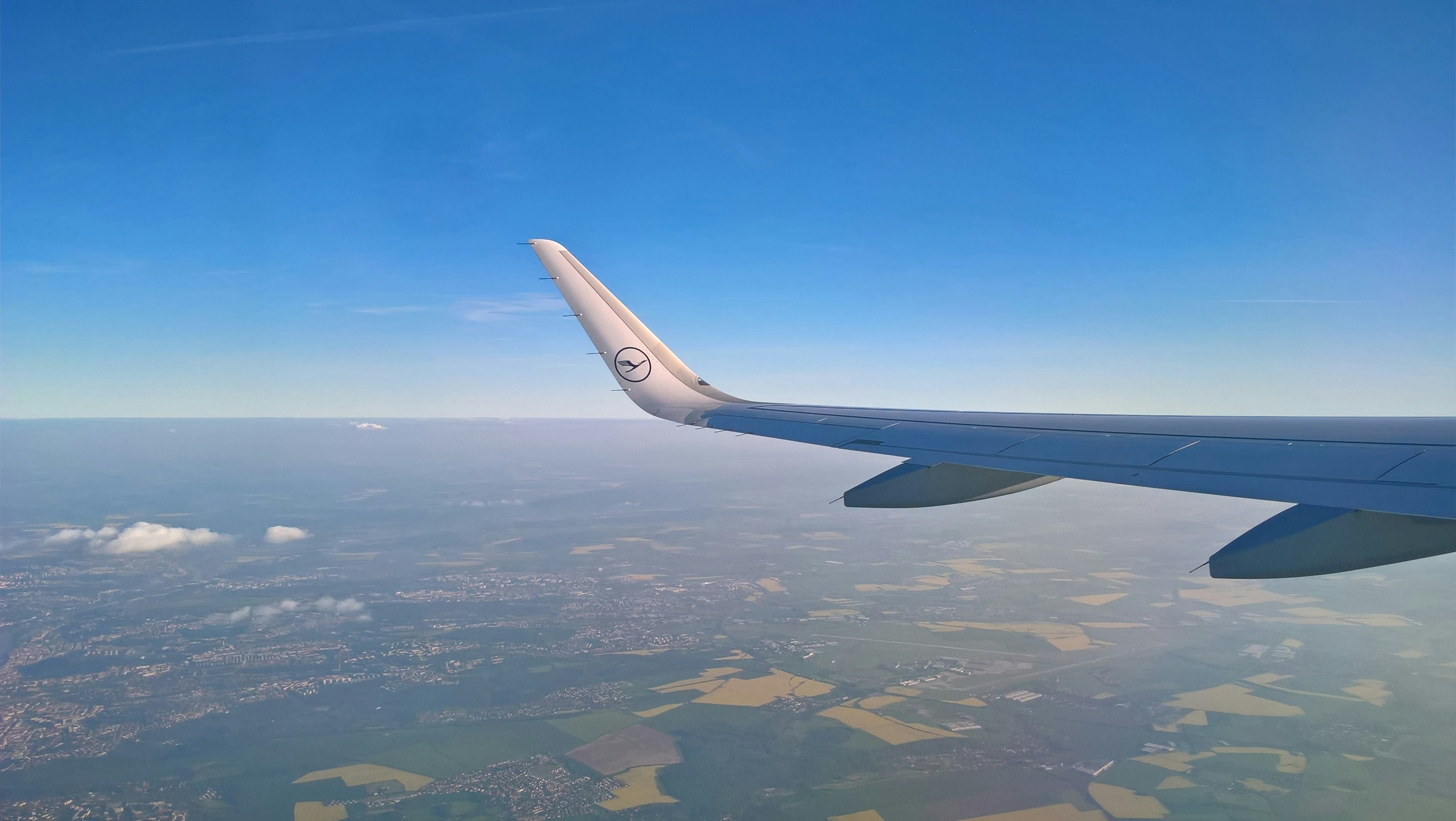 Airplane wing against a clear blue sky over land.