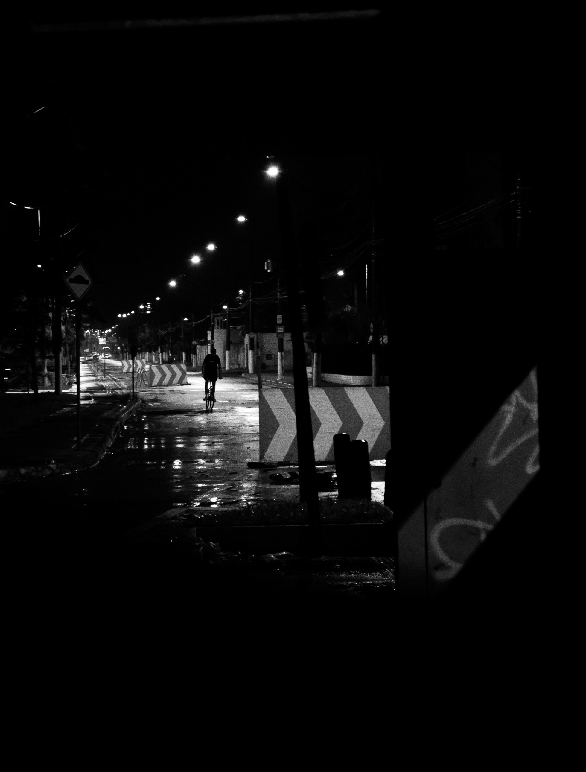 A lone cyclist rides on a wet street at night.