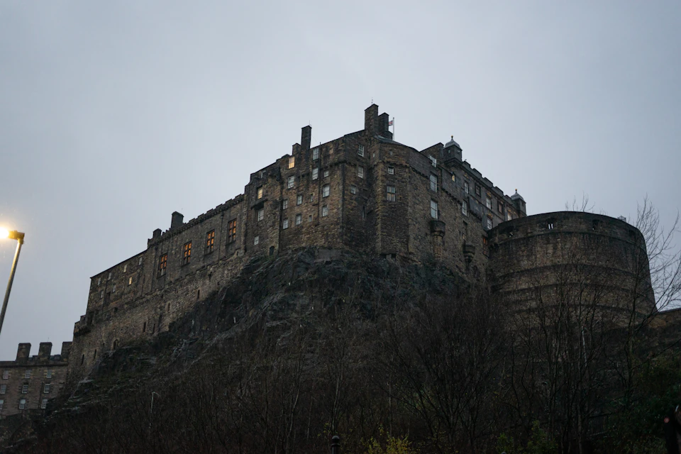 Gray stone castle atop rocky cliff with multiple towers and turrets against overcast sky