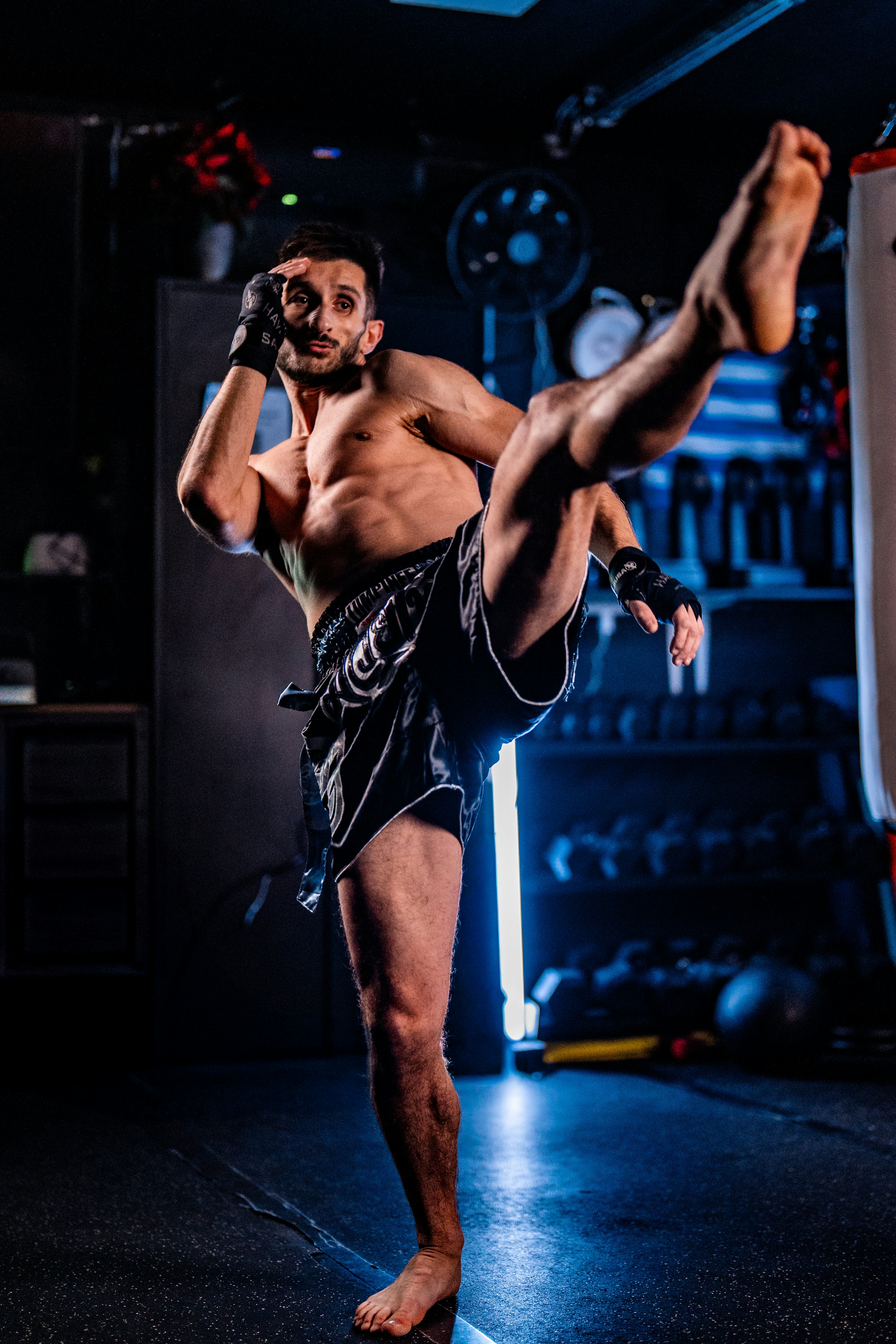 Man performing a dynamic kick in a dimly lit gym.