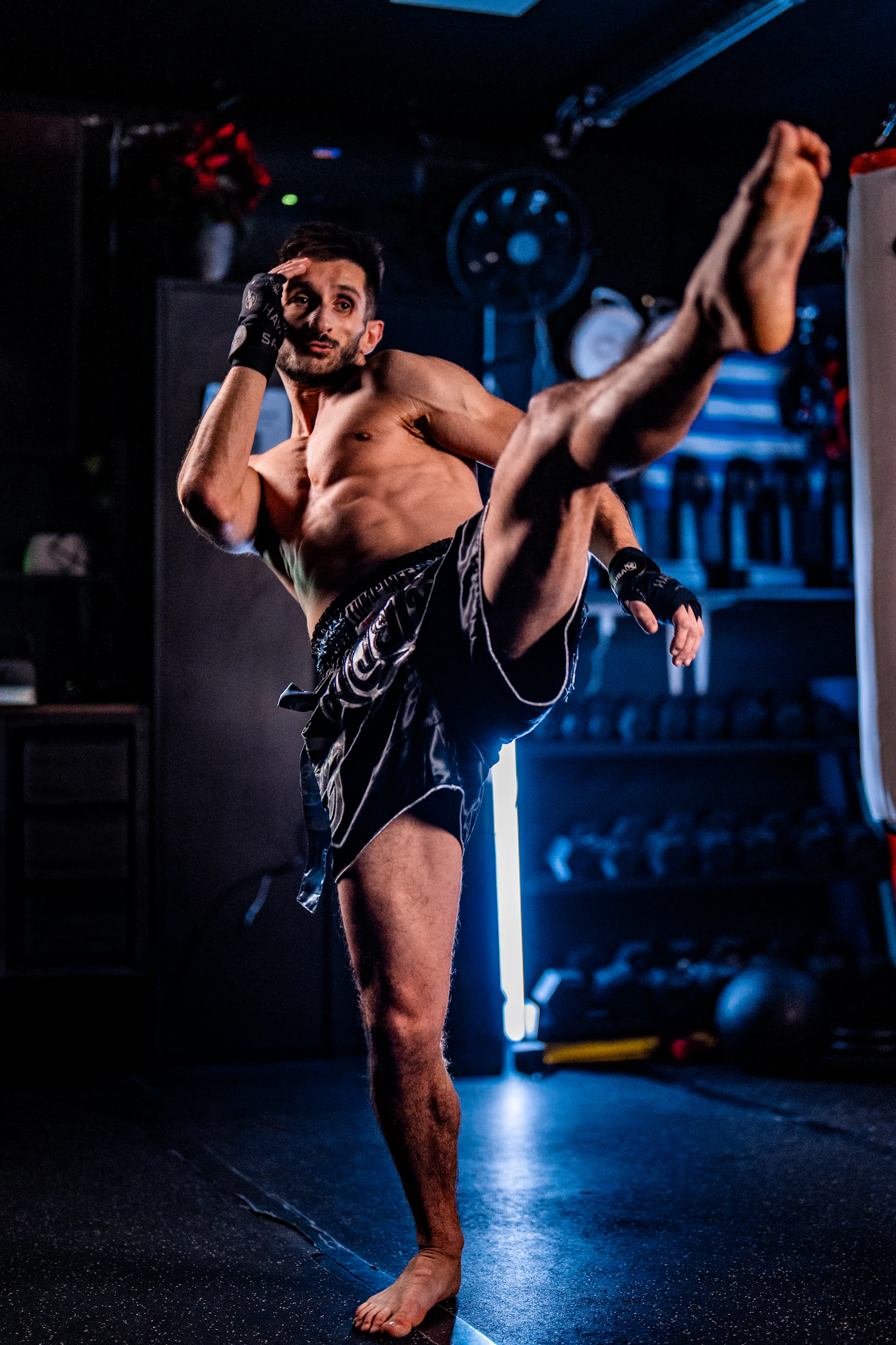 Artista marcial ejecutando una patada alta en un gimnasio con poca luz
