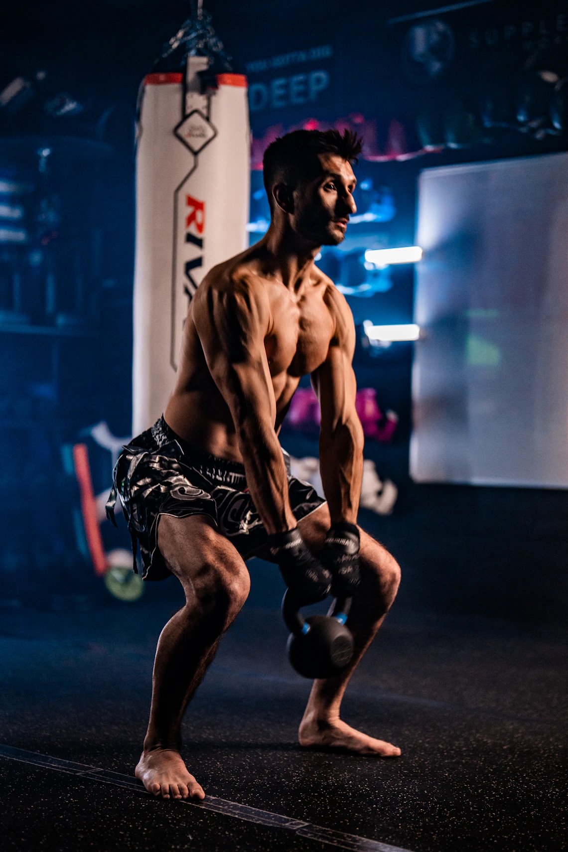 Athlete performing a powerful kettlebell movement inside a dark professional gym