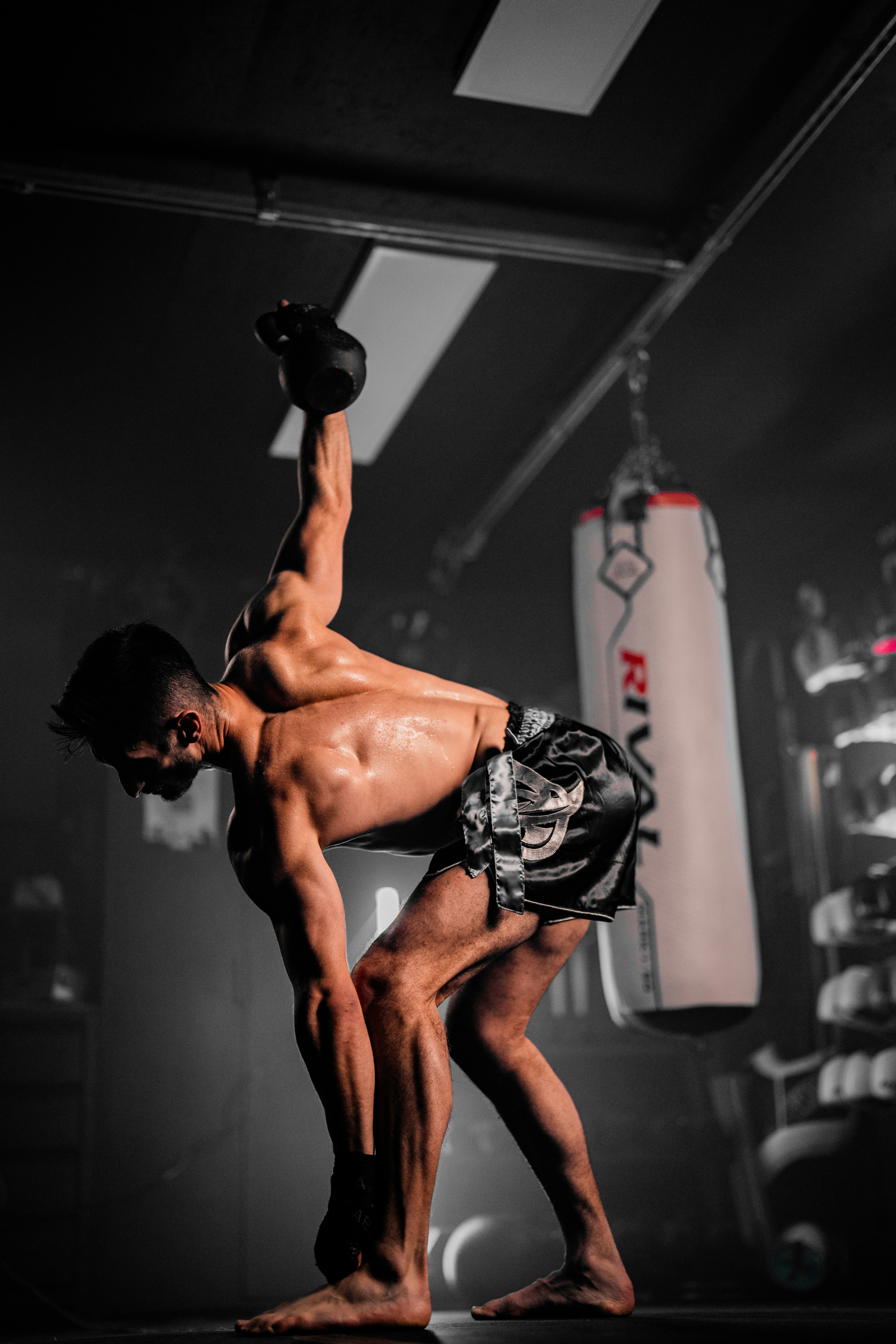 Man lifting kettlebell in dark gym with punching bag
