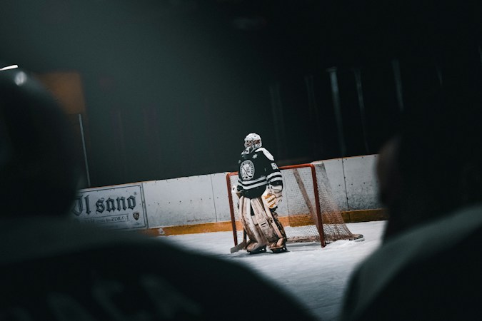 A hockey goalie in full gear stands near the net on the ice, guarding the crease during a game