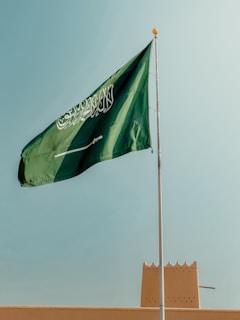 Saudi arabian flag waving against a clear blue sky.