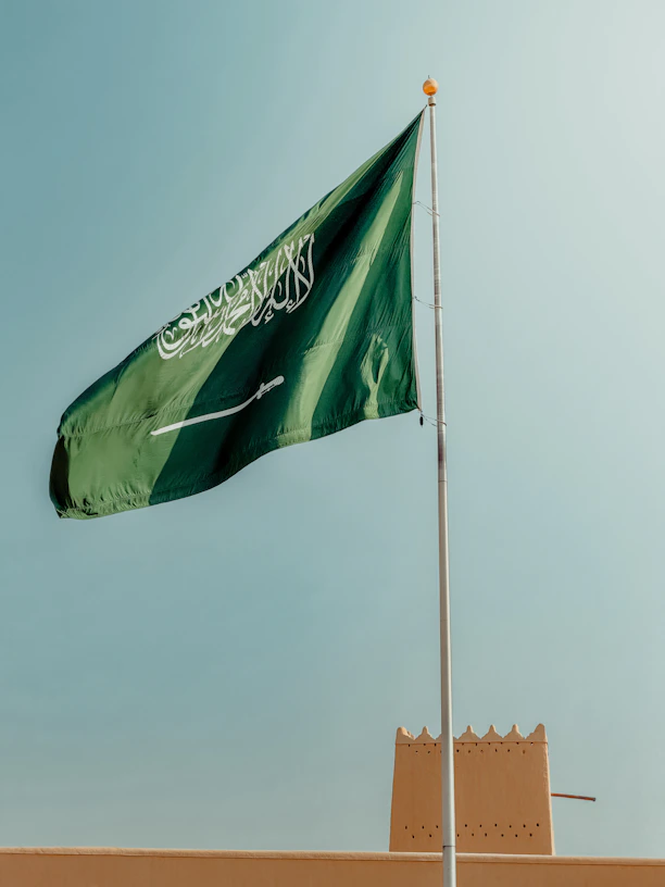 Saudi arabian flag waving against a clear blue sky.
