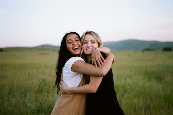 Two happy women hugging in a grassy field