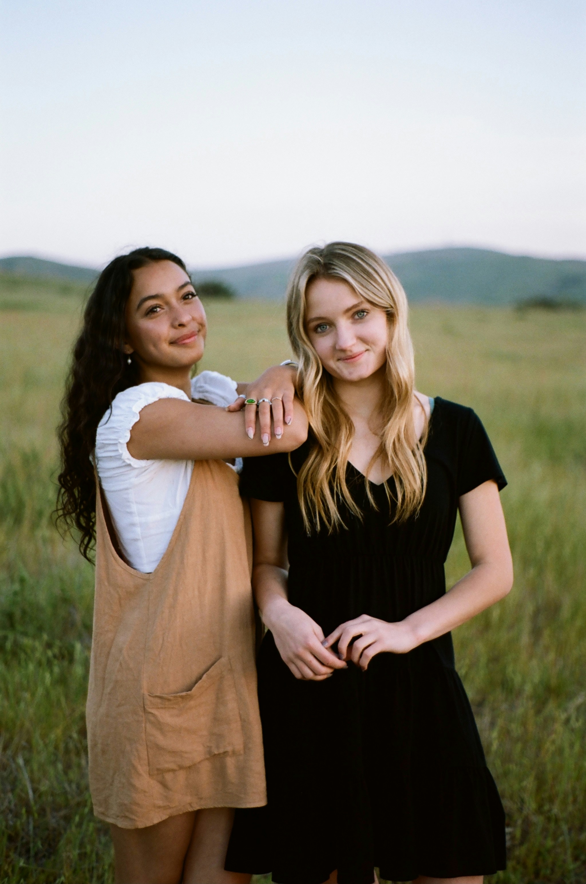 Two young women standing in a grassy field.