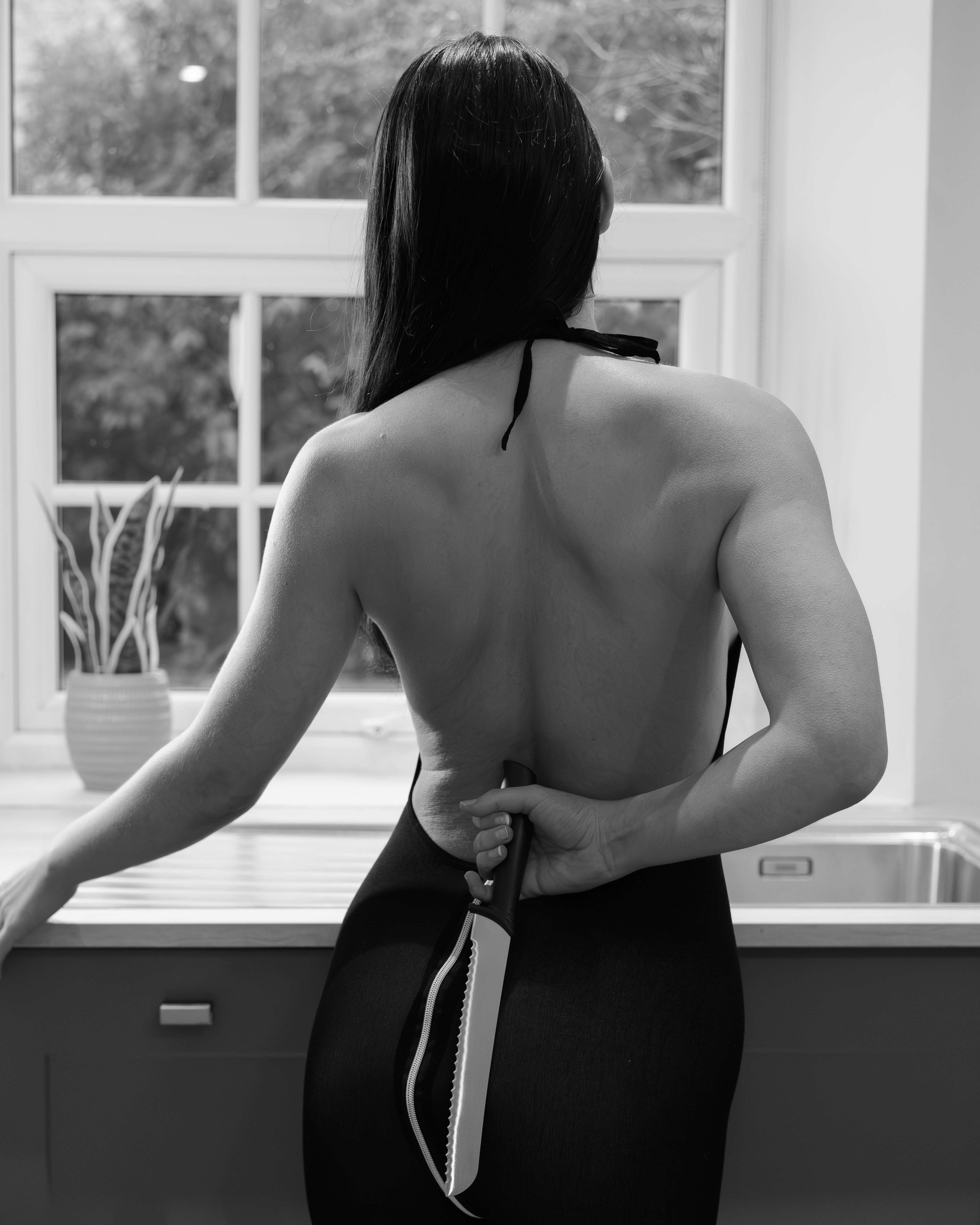 Woman holding knife behind back in kitchen.