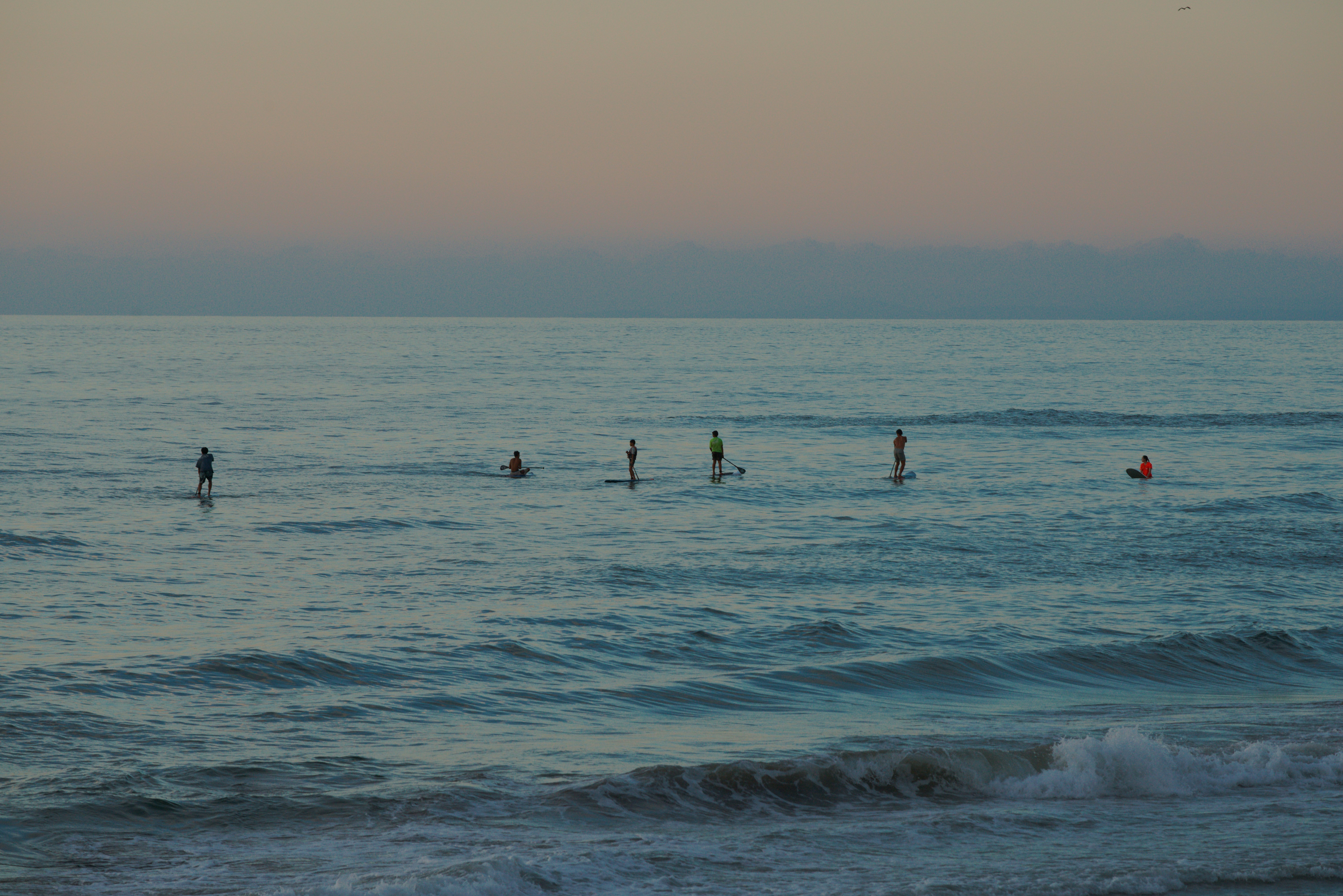 People paddleboarding on the ocean at dusk