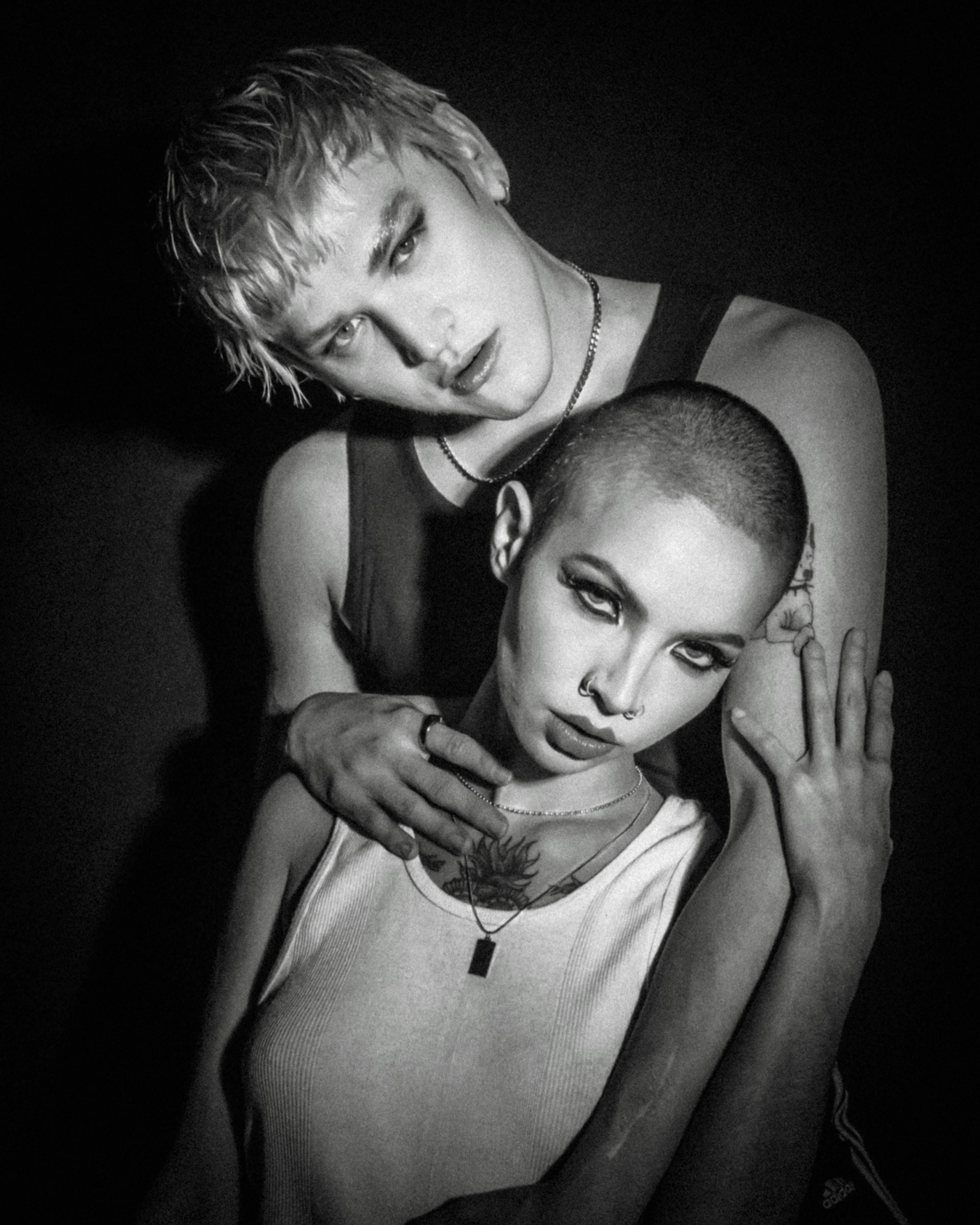 Two androgynous models pose intimately against dark background.