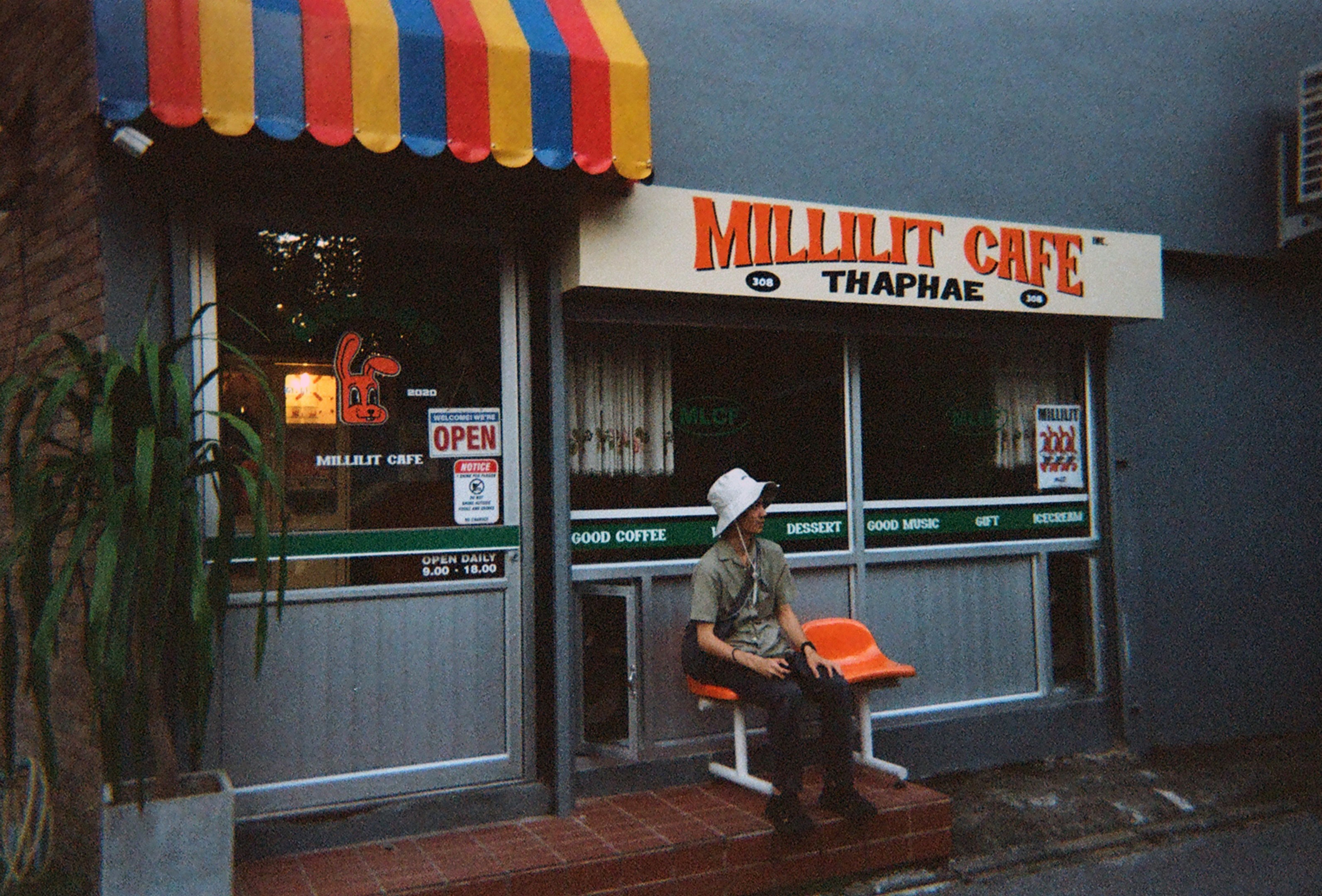 Man sits outside millilit cafe with striped awning.