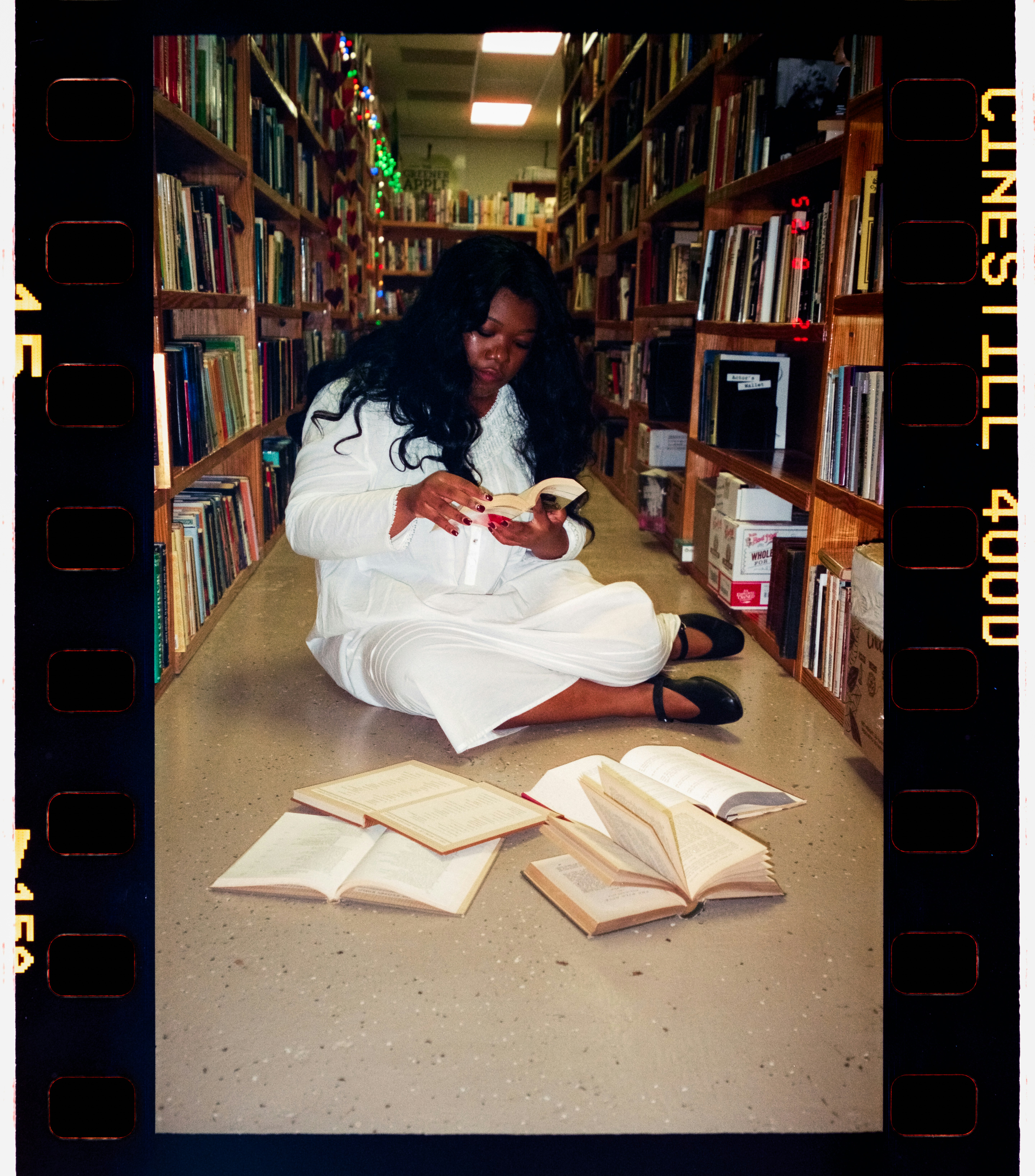 A woman reads a book in a library aisle.