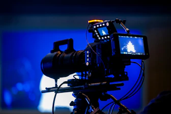 Professional video camera on tripod with blue background