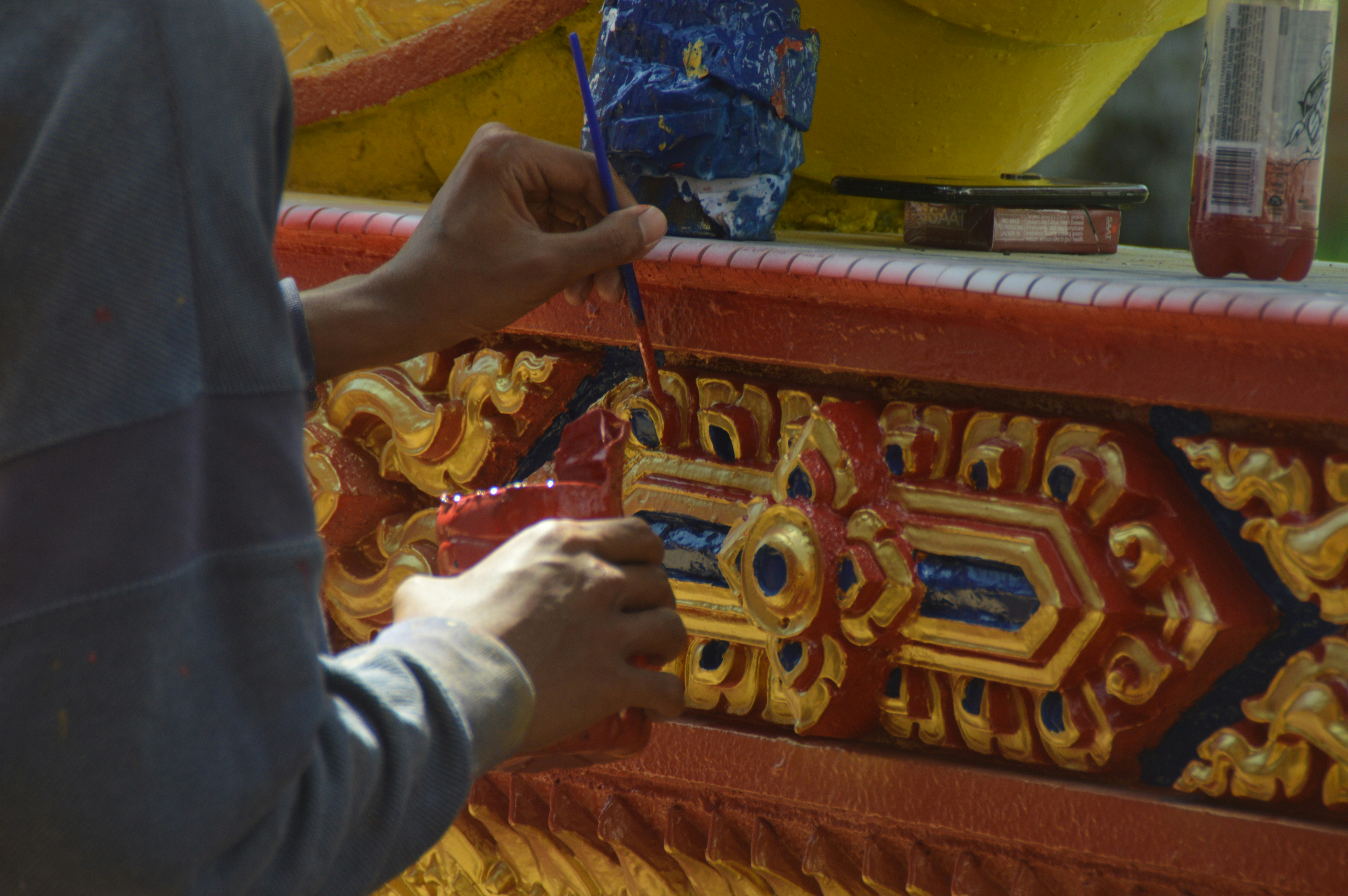 Artist hand painting intricate gold details on red surface.