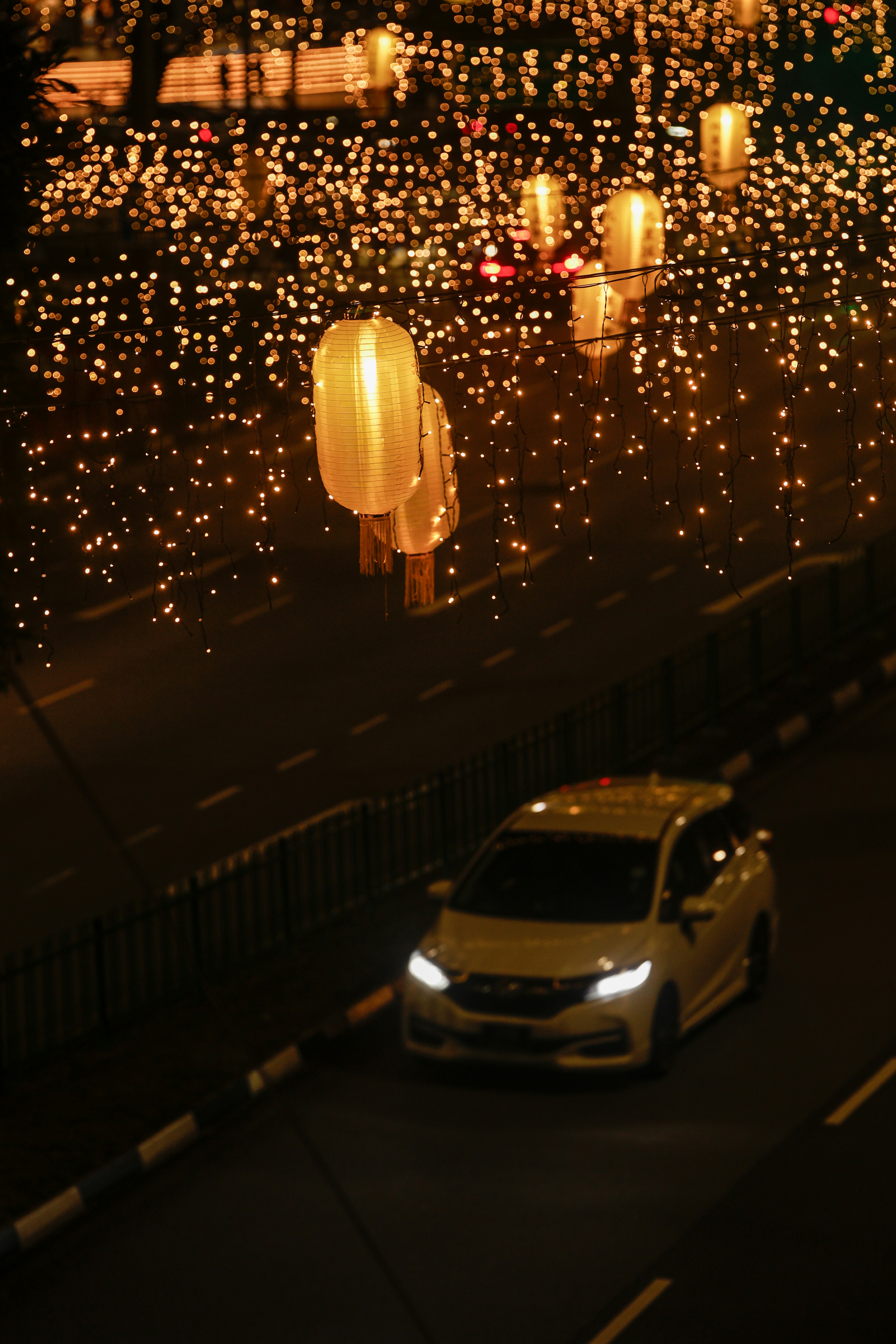 Car drives through street decorated with glowing lanterns