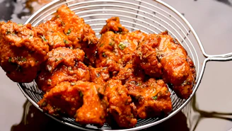 Crispy pakoras being drained in a metal strainer.