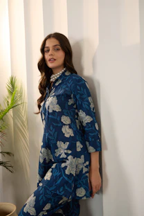 Woman in blue floral outfit leaning against wall