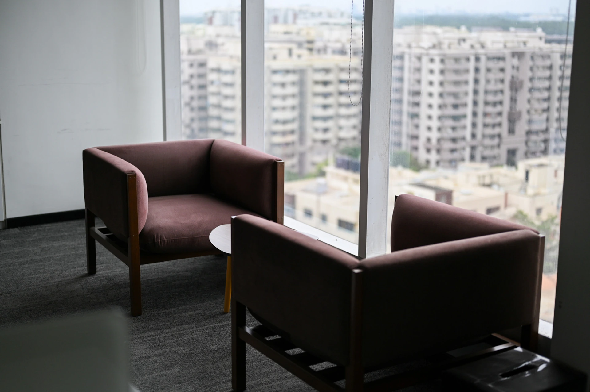 Two brown armchairs by a window overlooking city buildings.