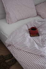 Red mug of coffee on a book in bed