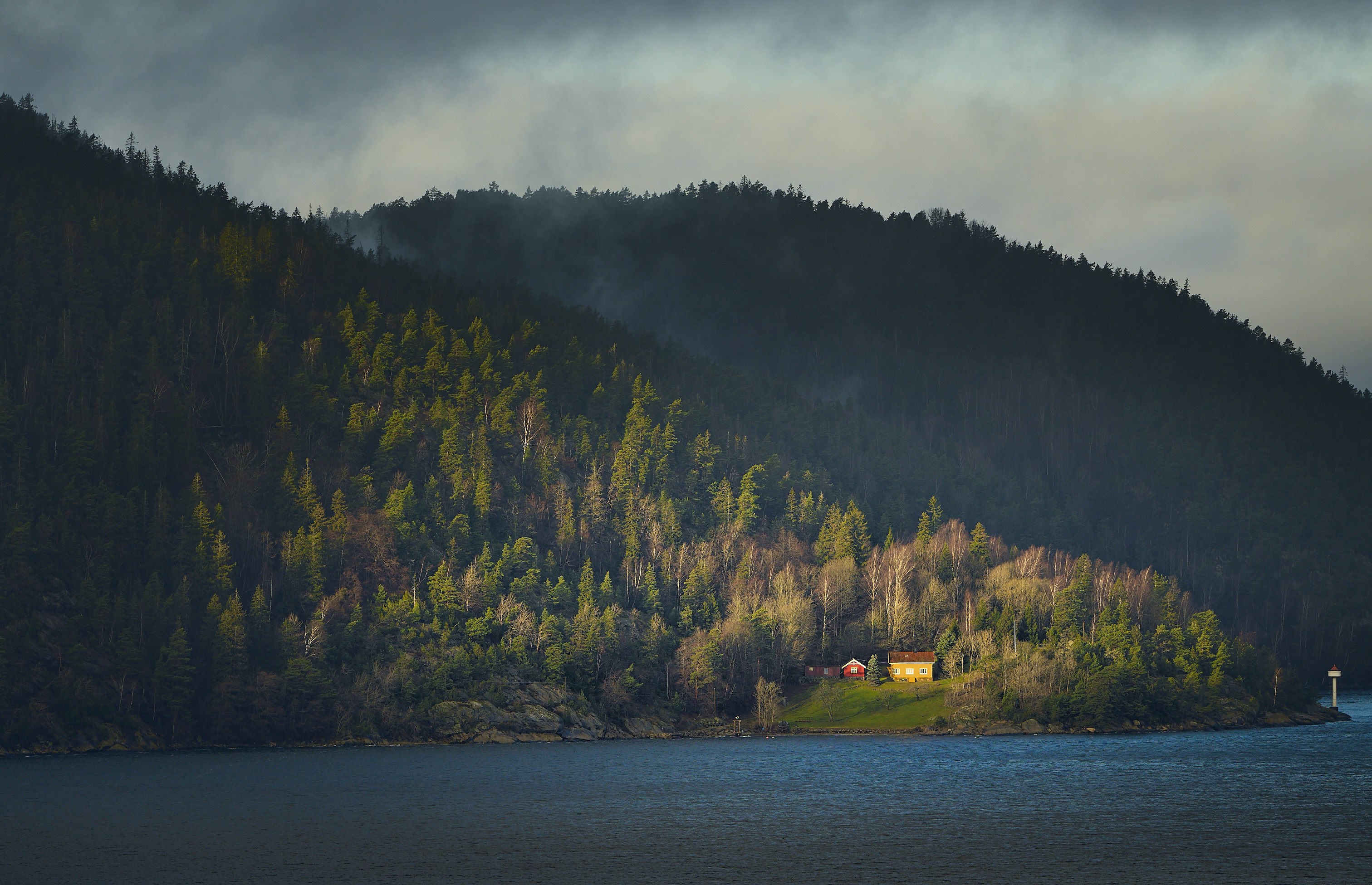 Small house and lighthouse on a forested island shore.