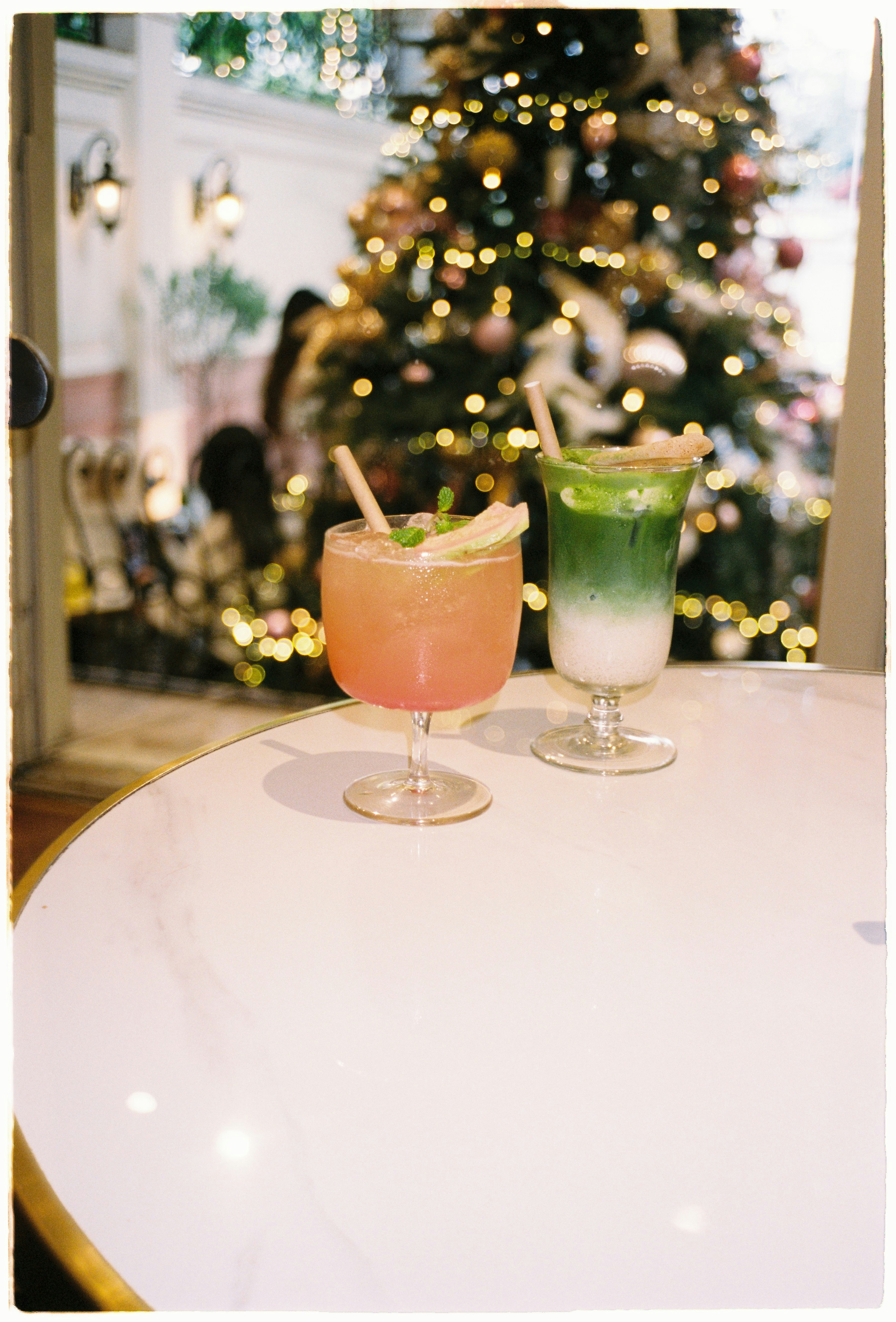 Two colorful drinks on a table near christmas tree.