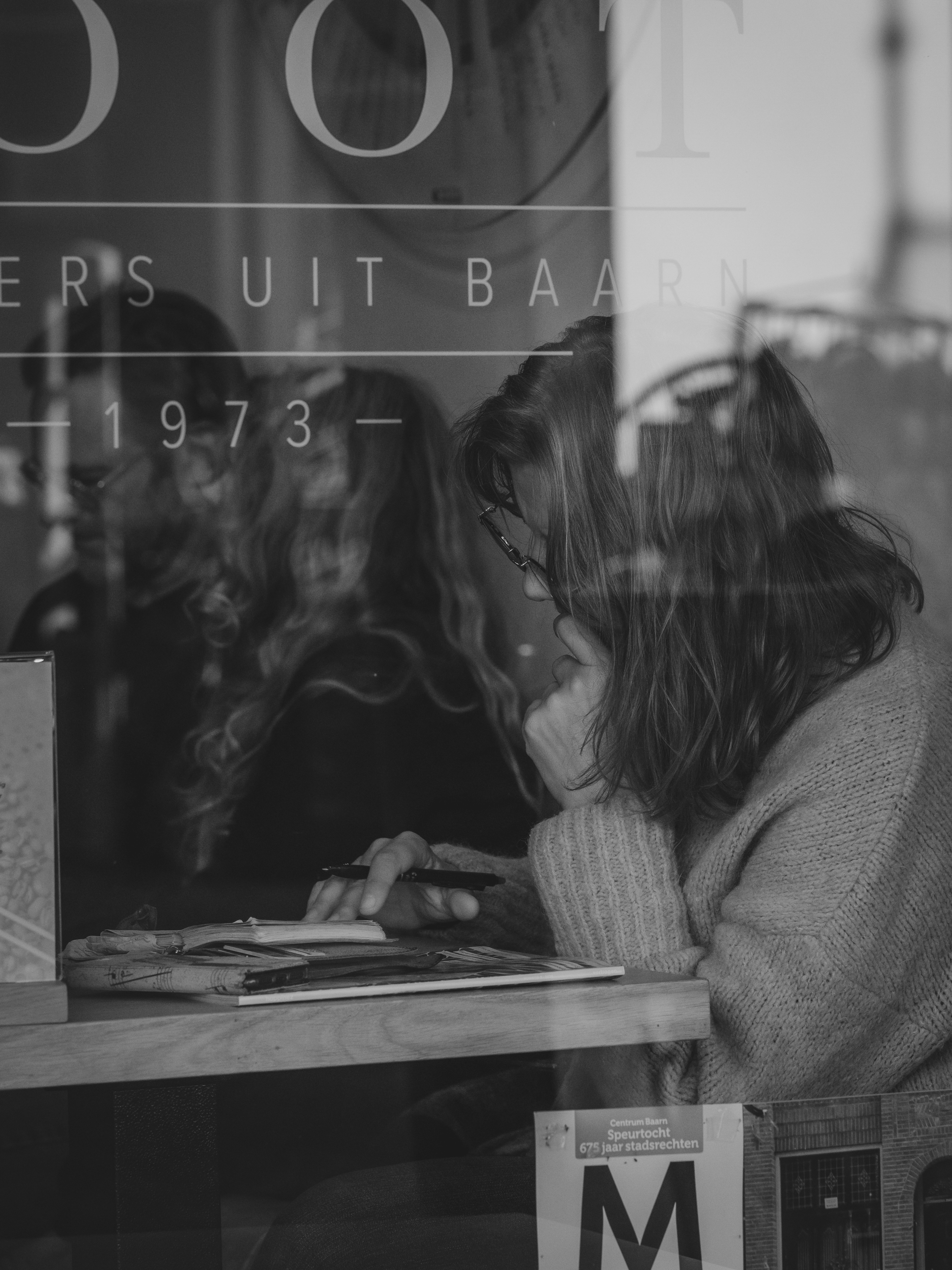 Two women looking at a book through window