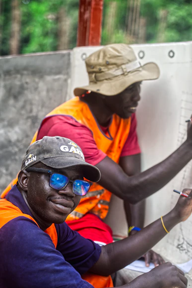 Two men wearing hats and vests writing on paper.