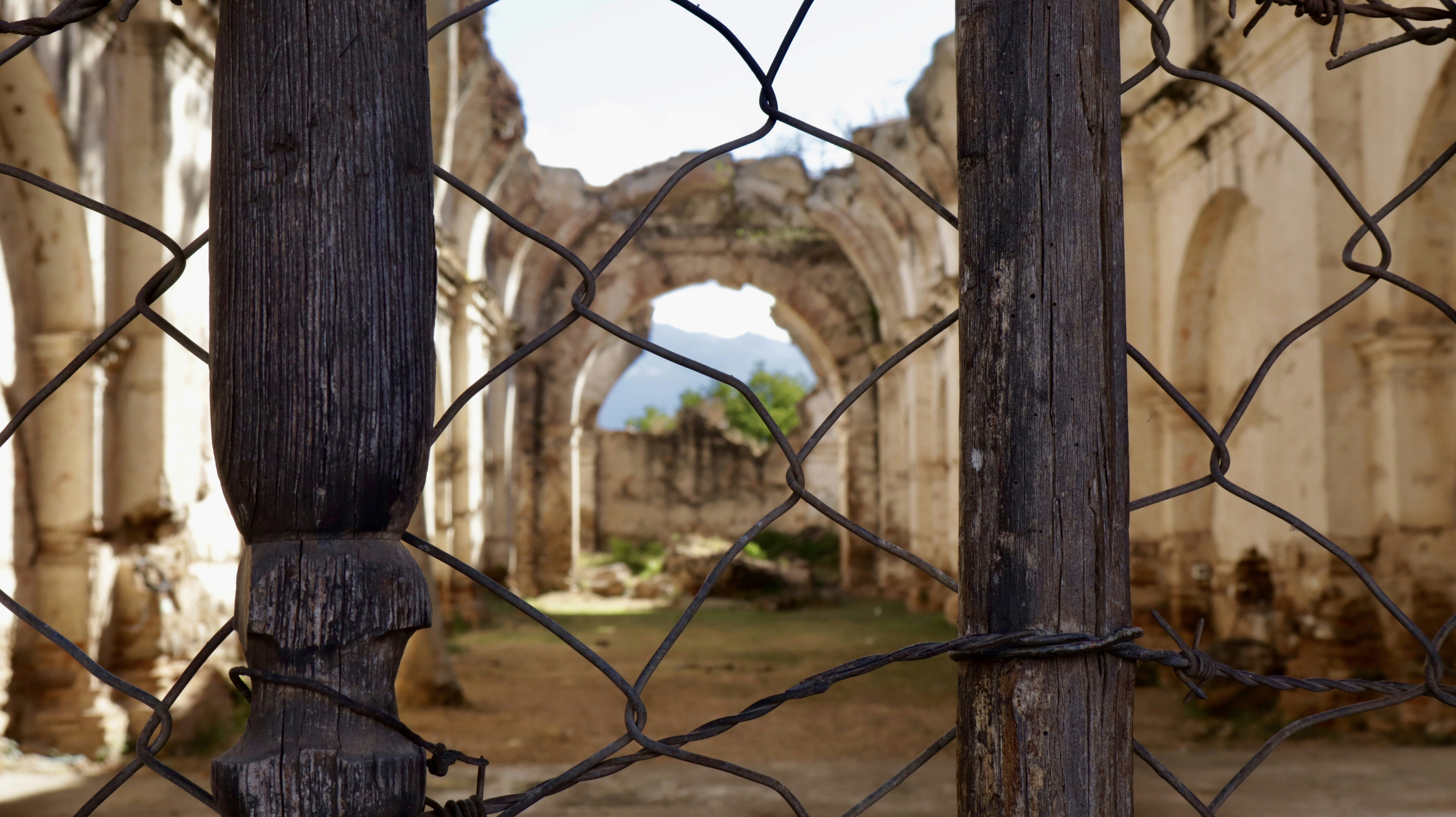 Ruined church interior seen through a wire fence.