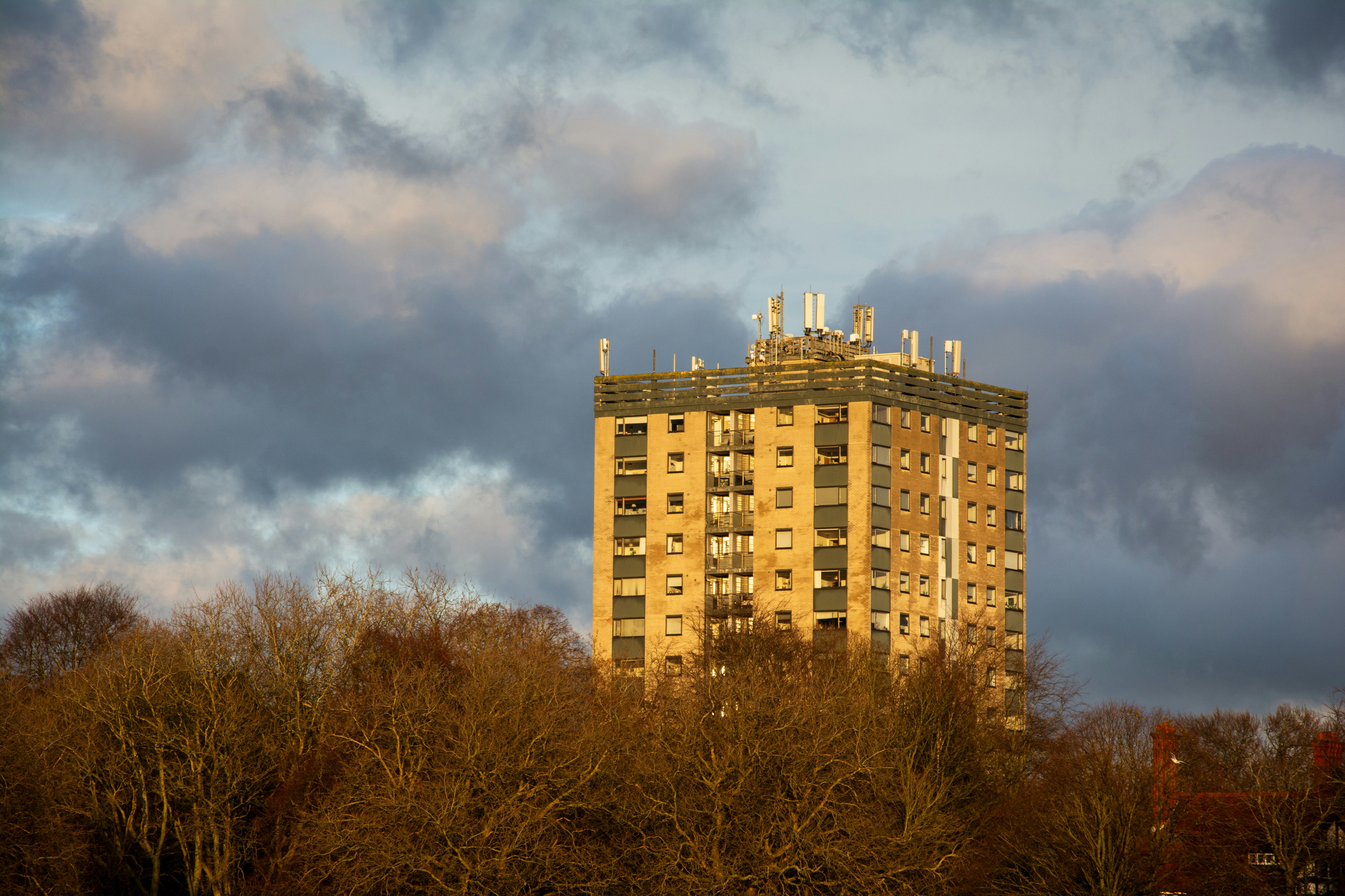 Tall apartment building behind bare trees and clouds.