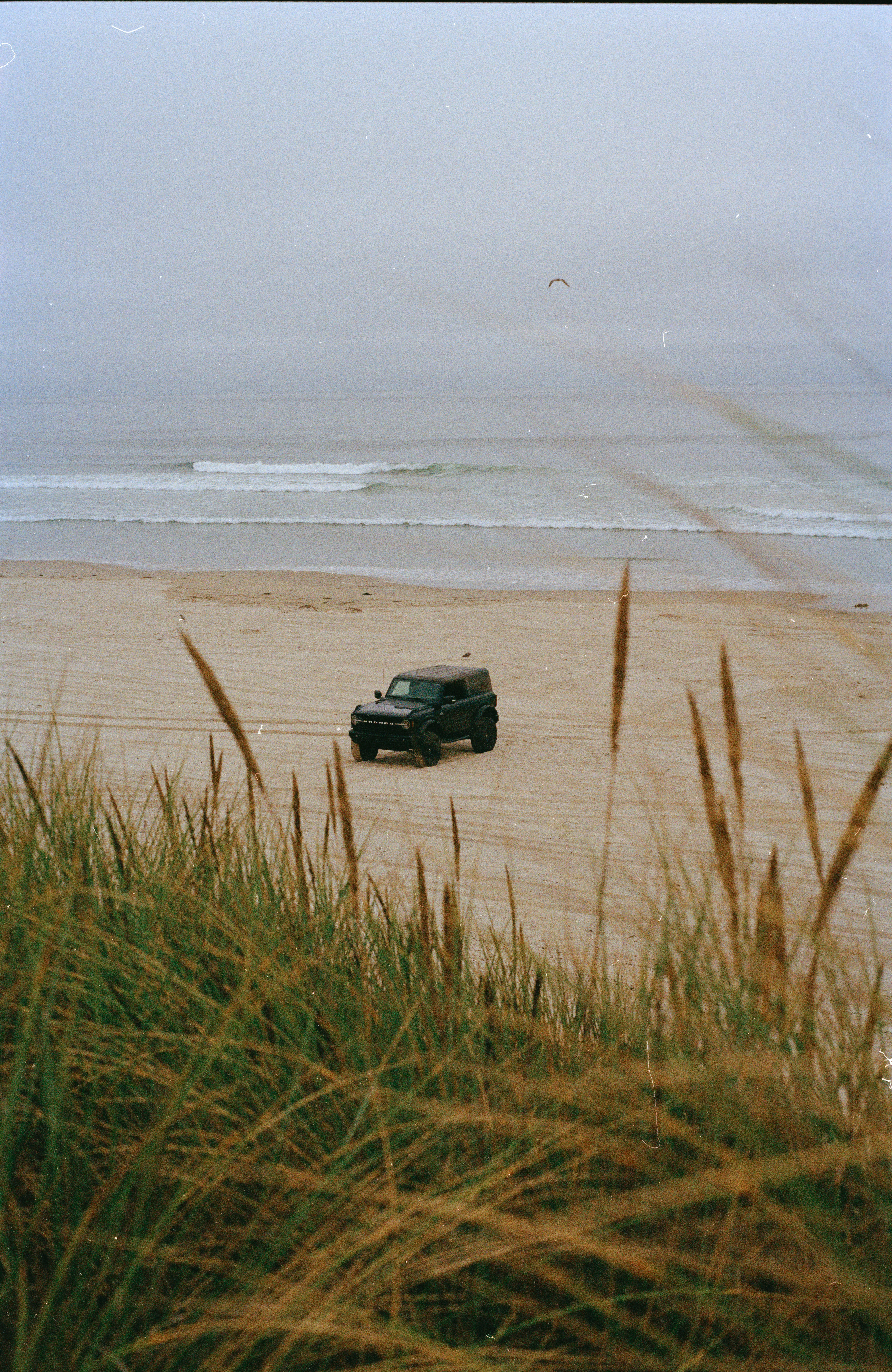 Dark suv parked on a sandy beach near ocean waves.