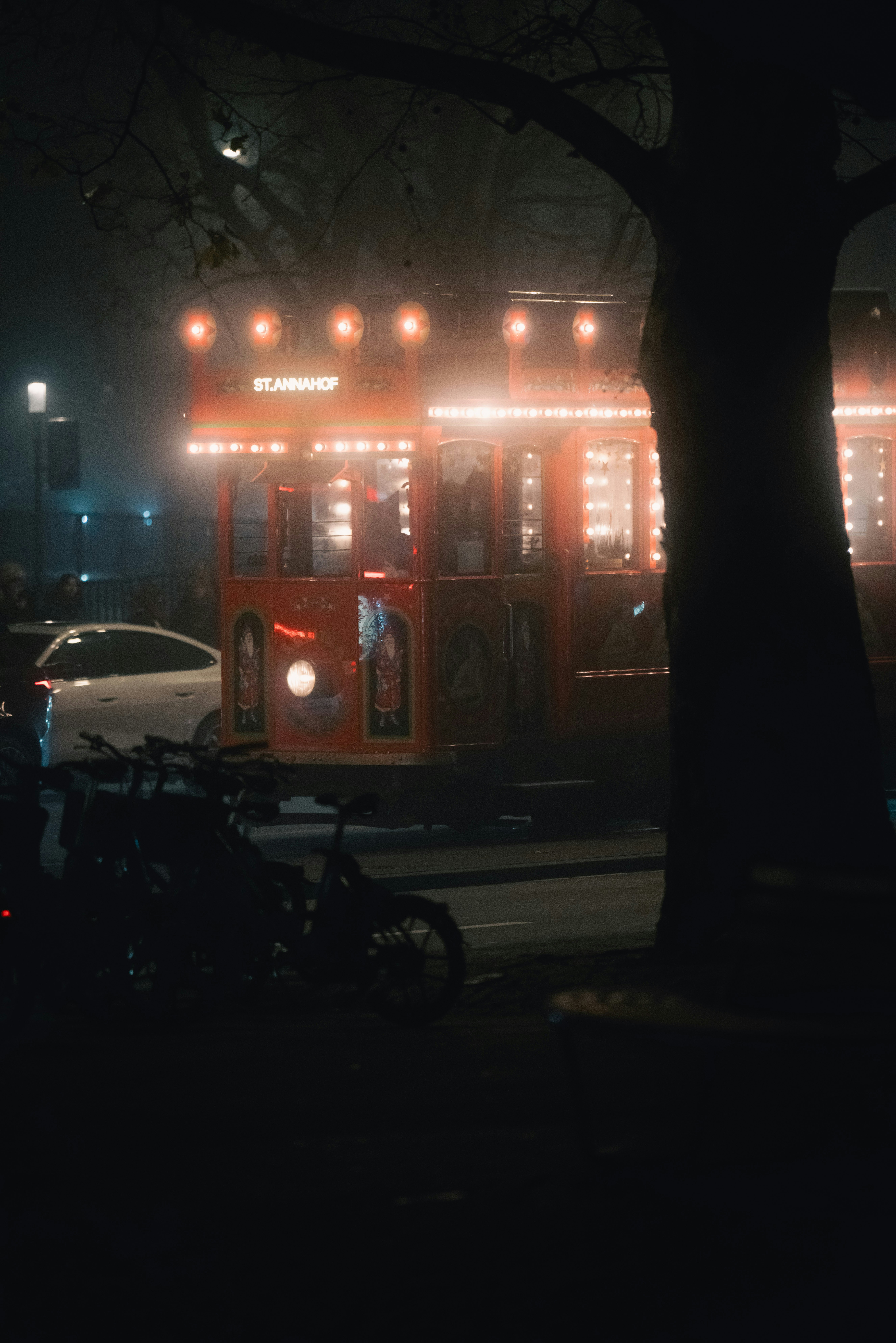 Red trolley car illuminated at night with parked bicycles