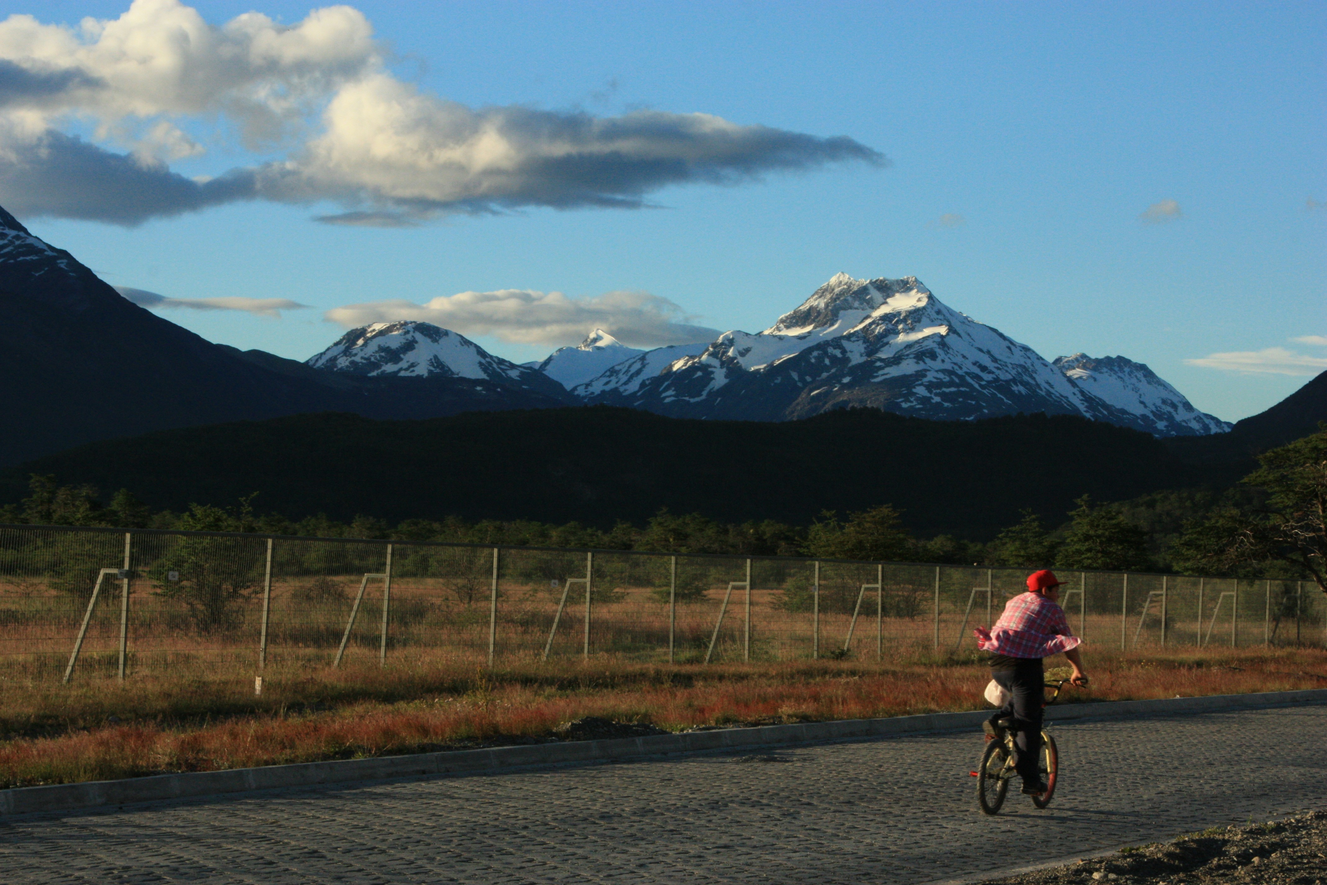 Person cycling on a road with snowy mountains behind.